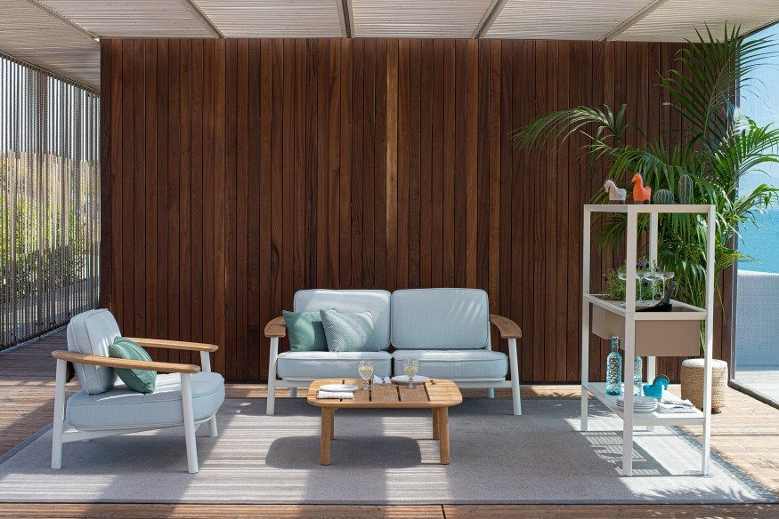 Helles Outdoor-Lounge-Set mit Sofa, Sessel und Beistelltisch auf einer Terrasse mit Holzverkleidung.