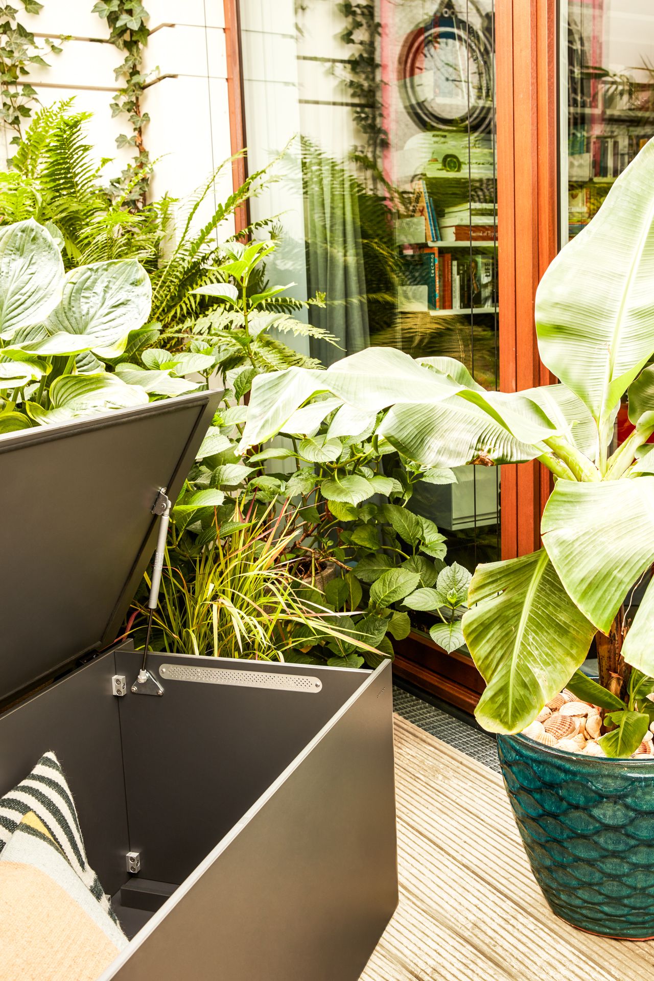EL Pecho Kissentruhe von Conmoto, geöffnet, mit Kissen auf einer Terrasse mit Pflanzen.