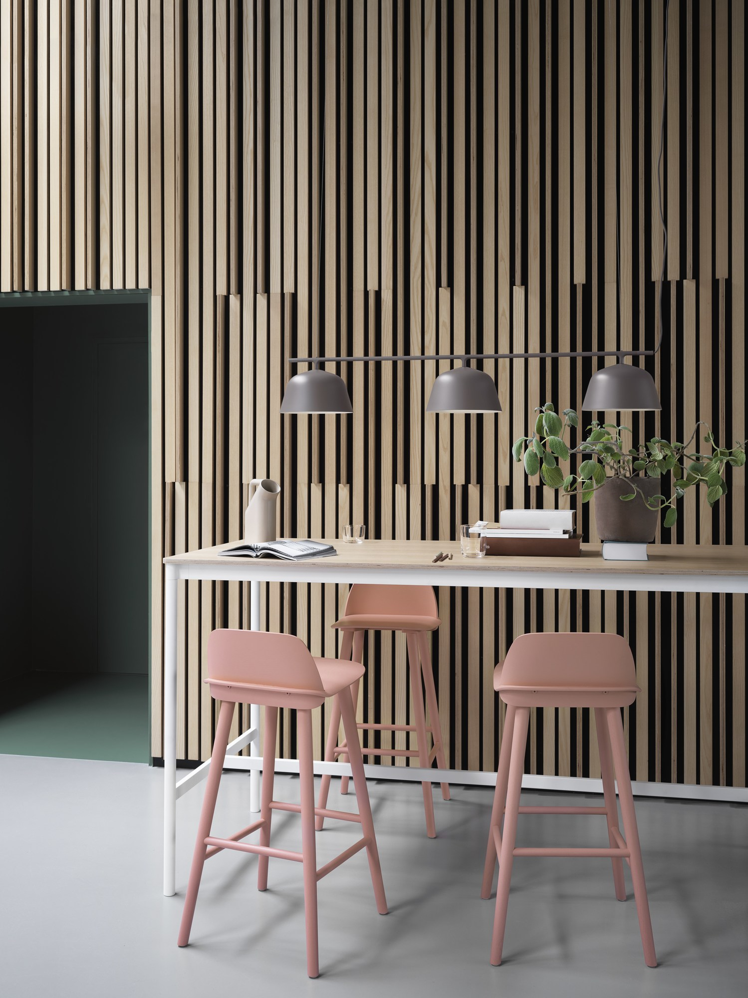 Graue Muuto Rail Lamp Pendelleuchte über Esstisch mit rosa Barhockern und Holzpaneelen.