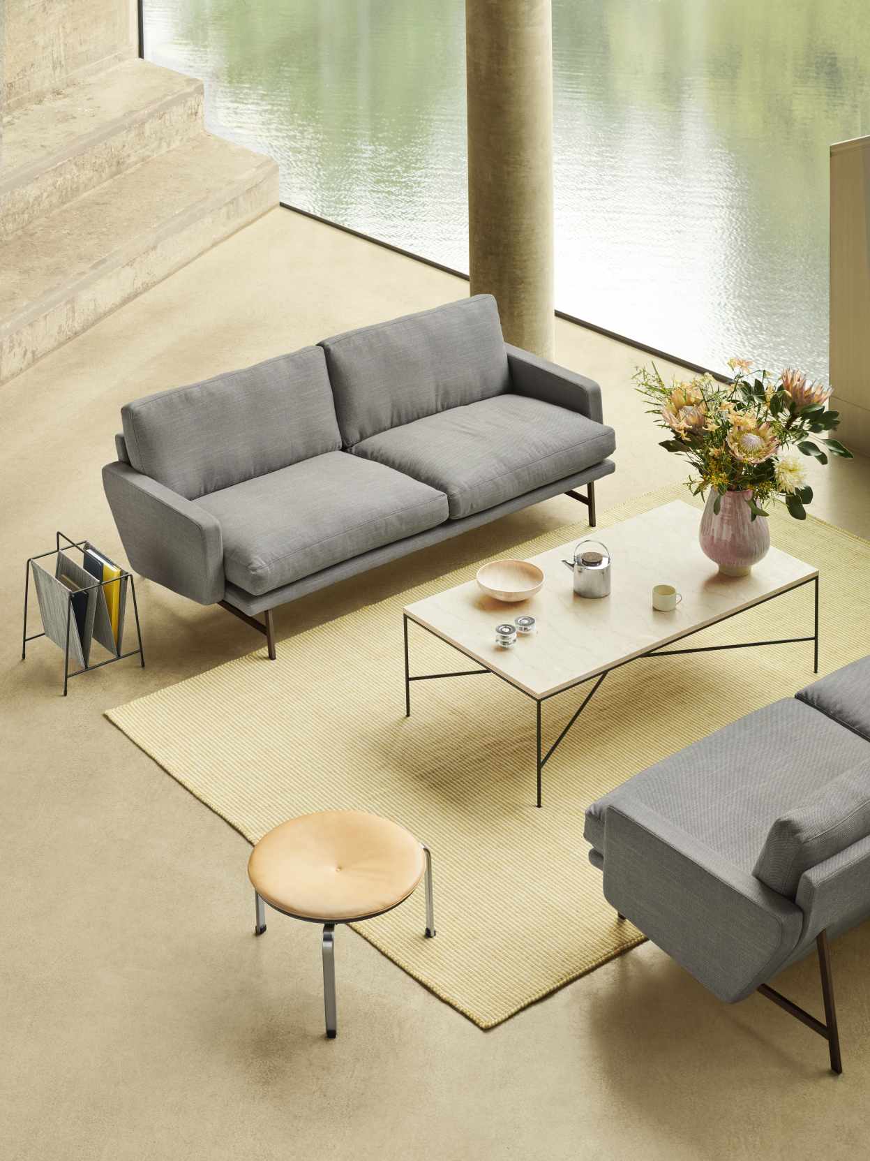 Helle Wohnzimmer-Szene mit grauem Sofa, Fritz Hansen Couchtisch Planner und Dekoration auf beigem Teppich.