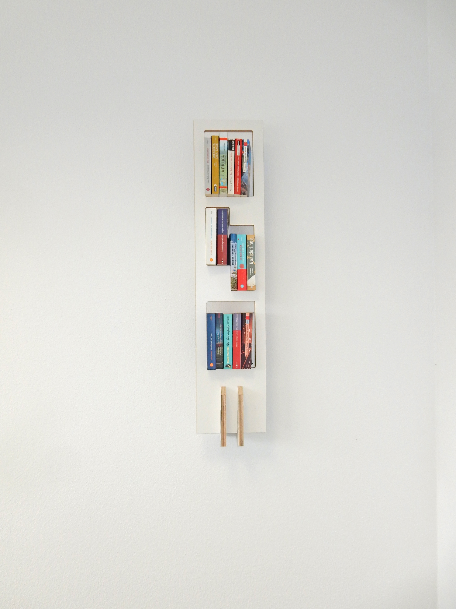 Weißes Tojo Lesestoff Bücherregal an einer weißen Wand mit bunten Büchern gefüllt.
