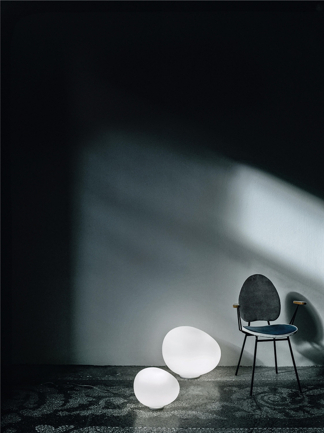 Zwei Gregg Bodenleuchten von Foscarini neben einem Stuhl, stimmungsvolle Beleuchtung für den Außenbereich.