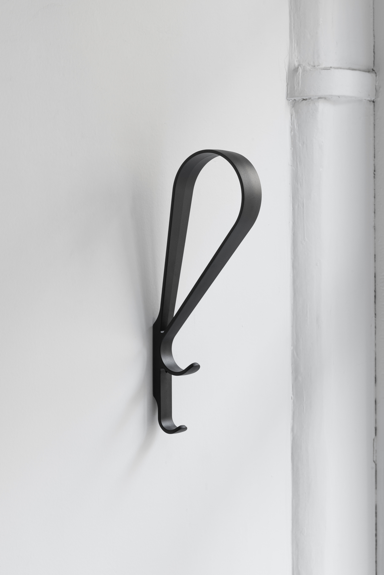 Schwarzer Artek Tupla Wandhaken an einer weißen Wand, minimalistisches Design für Garderobe oder Bad.