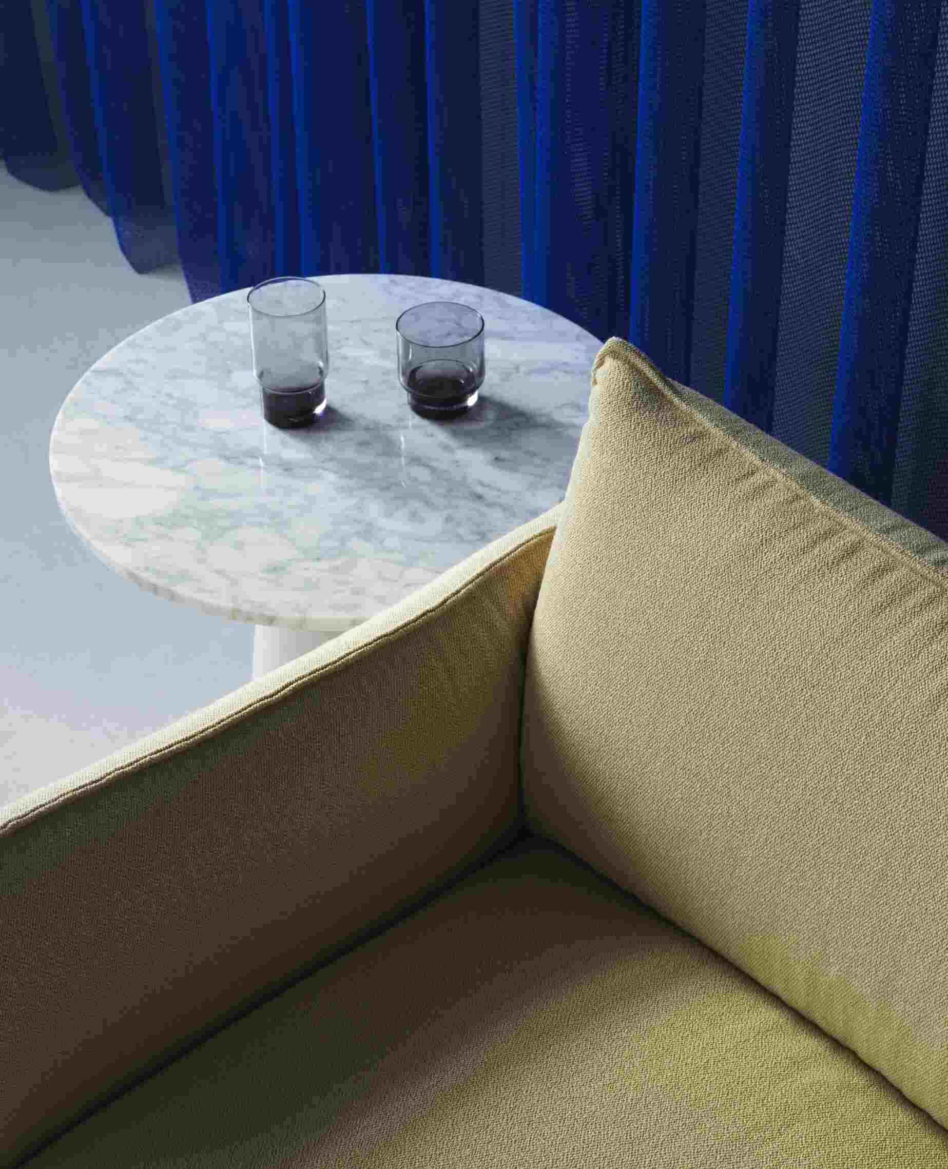 Nahaufnahme des Ark Lounge Chair Sessels von Normann Copenhagen in Beige mit Marmortisch und Gläsern.