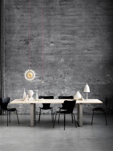 Fritz Hansen Essay Tisch mit Stühlen und Dekoration vor einer grauen Wand.