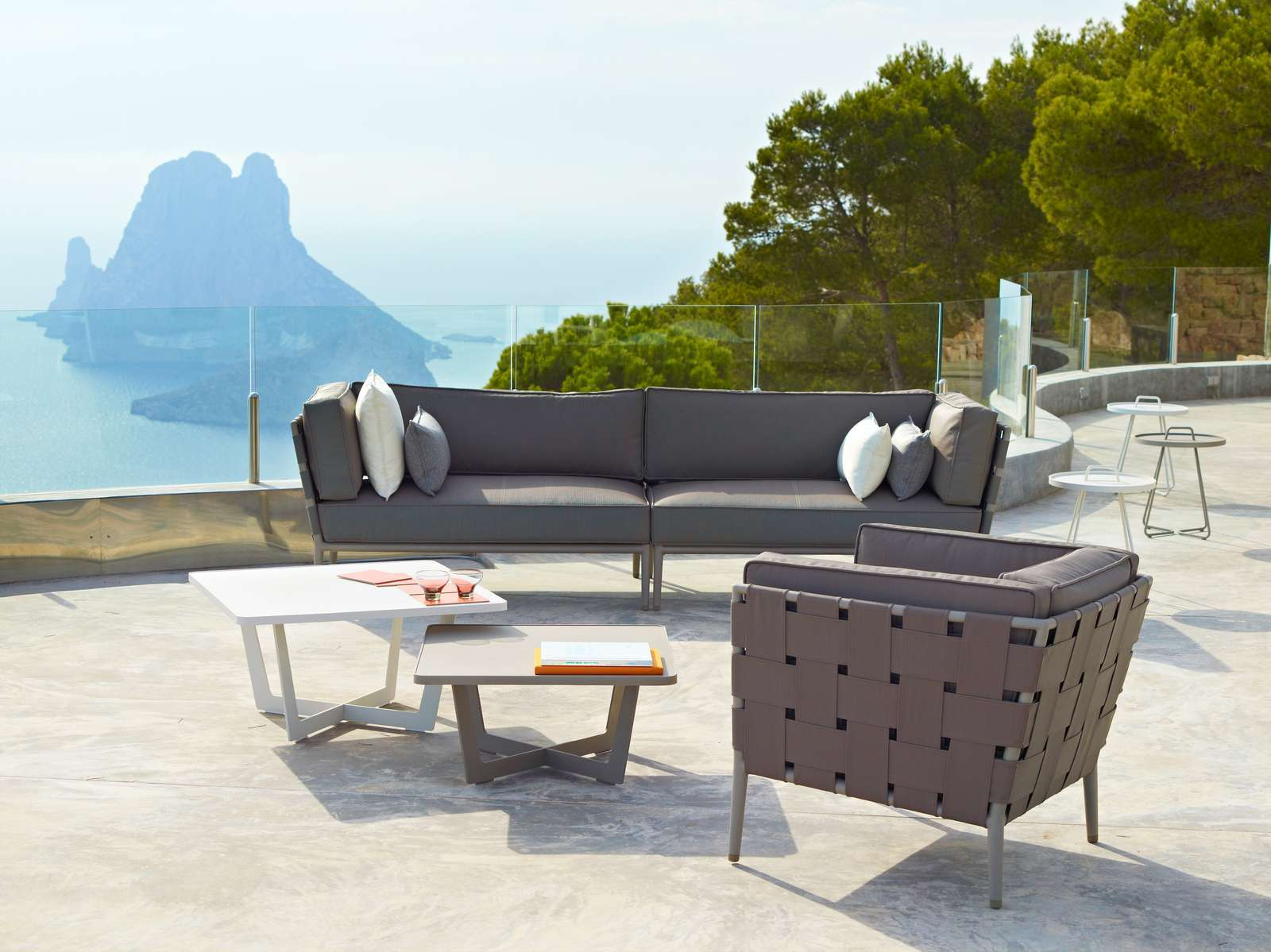 Conic Outdoor Sofa von Cane-Line, graues 2-Sitzer Modulsofa mit Kissen und passendem Loungesessel auf Terrasse.
