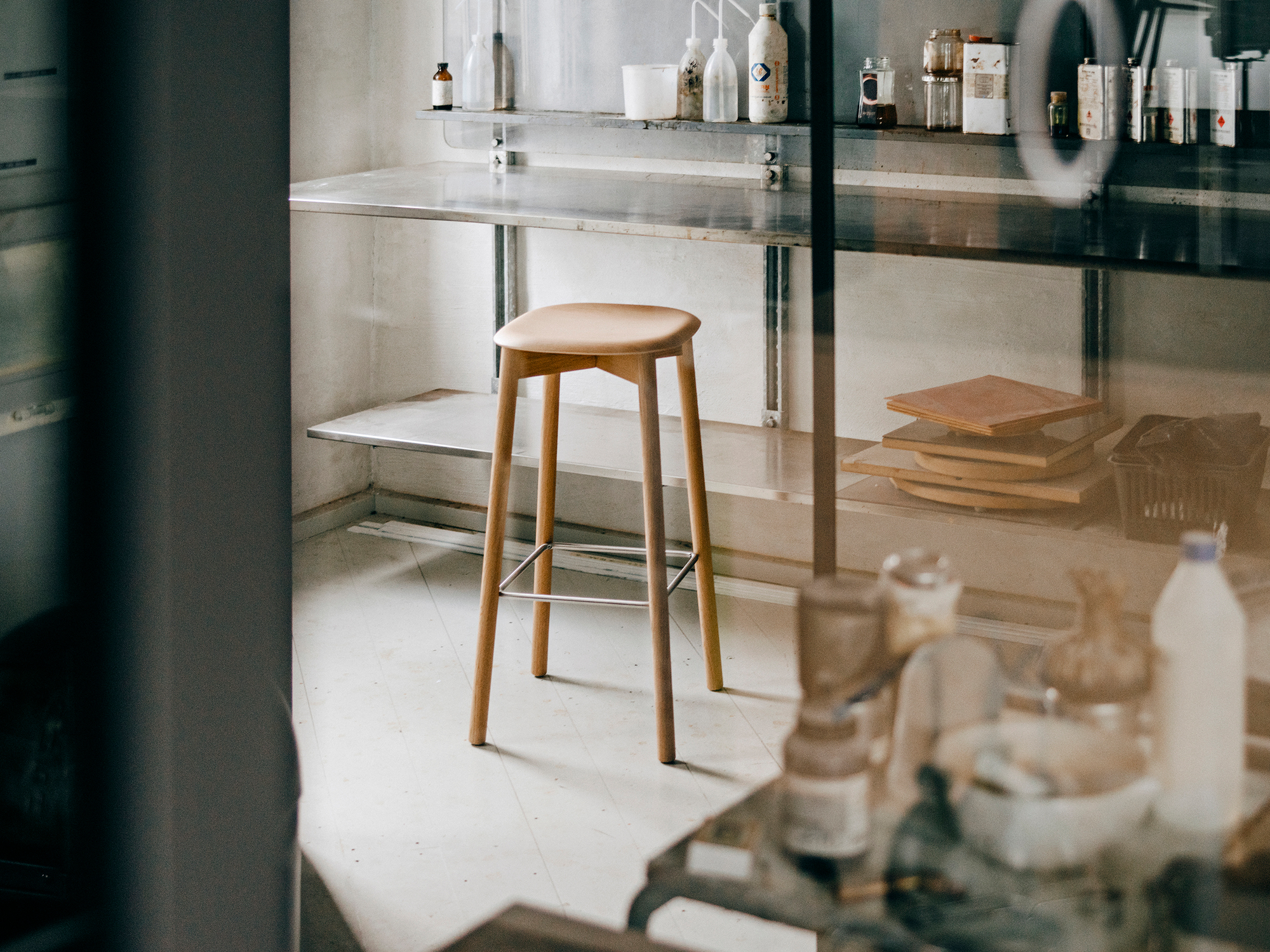 Holzhocker "Soft Edge" von Hay mit Fußstütze vor Regalen in Werkstatt-Atmosphäre.