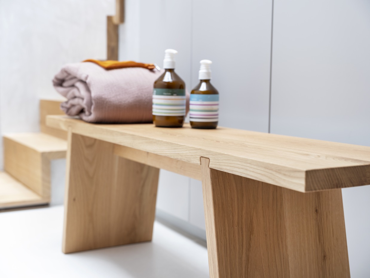 Helle Holzbank mit Handtuch und Seifenspendern. Dovetail Bank für Badezimmer und Wohnbereich.