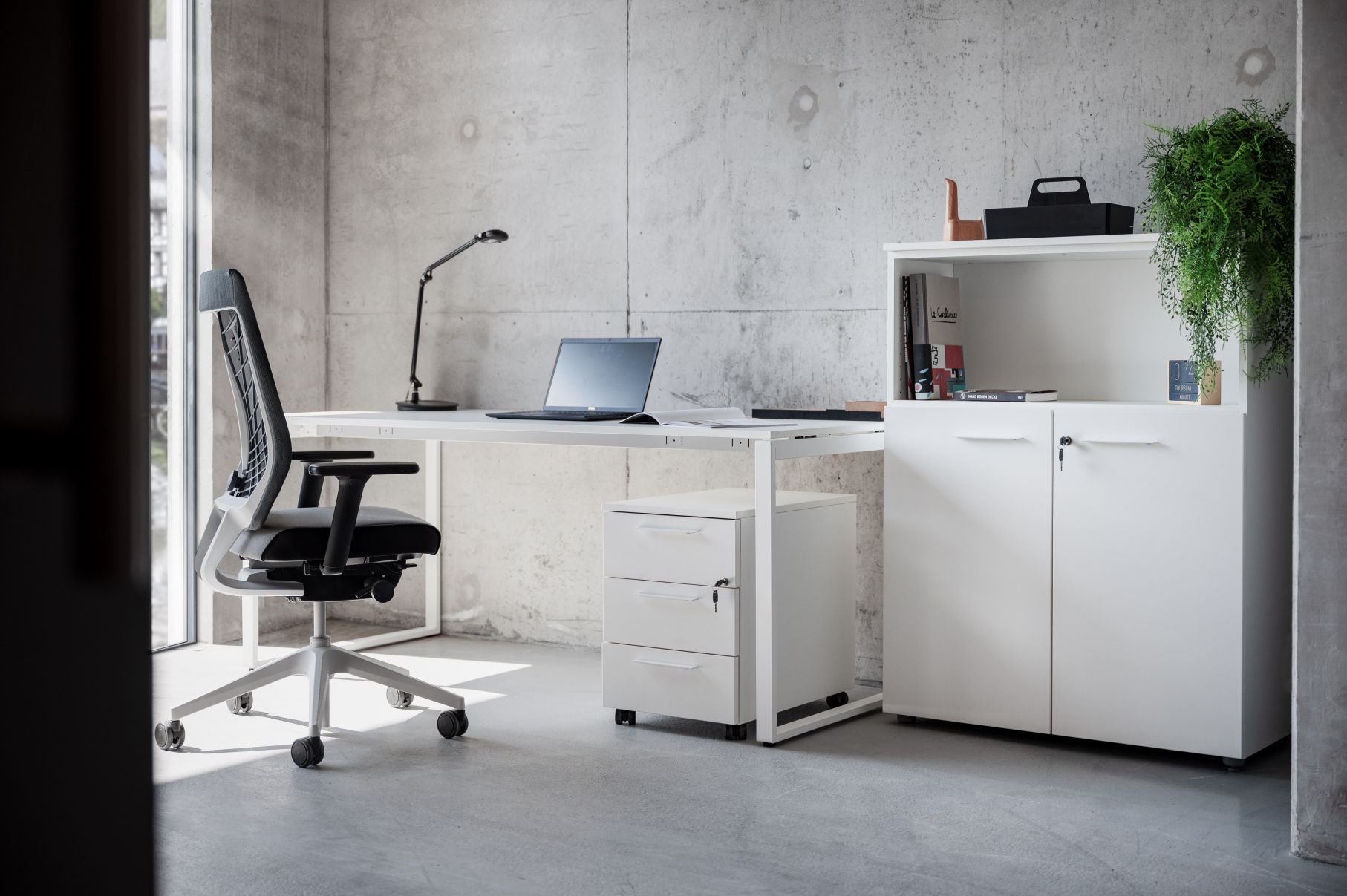 Weißer Frezza Rollcontainer Pedestal MET unter Schreibtisch im modernen Büro mit Betonwand. Büromöbel für mehr Stauraum.