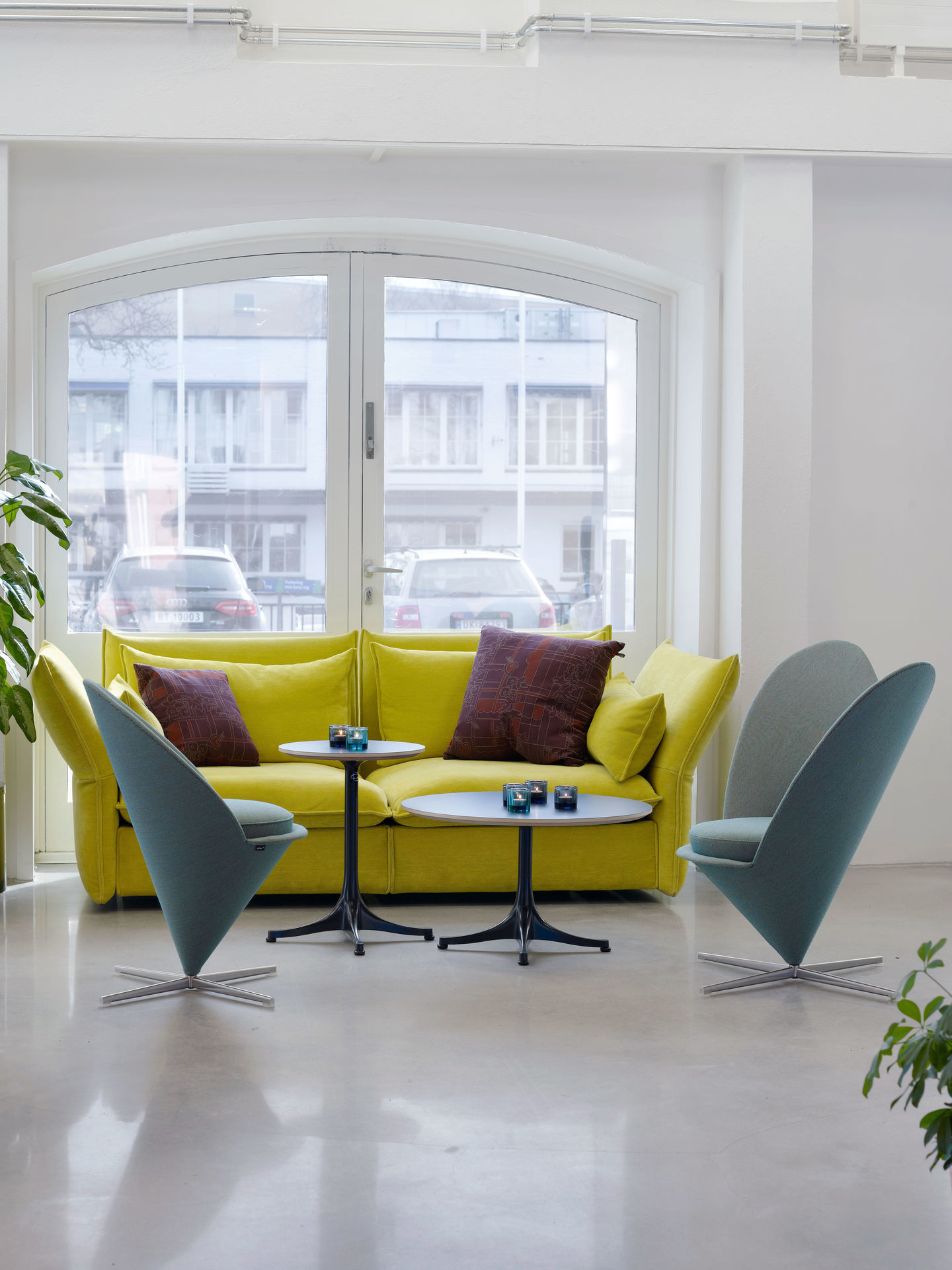 Innenaufnahme mit gelbem Sofa, zwei Heart Cone Chairs von Vitra und kleinen Tischen.