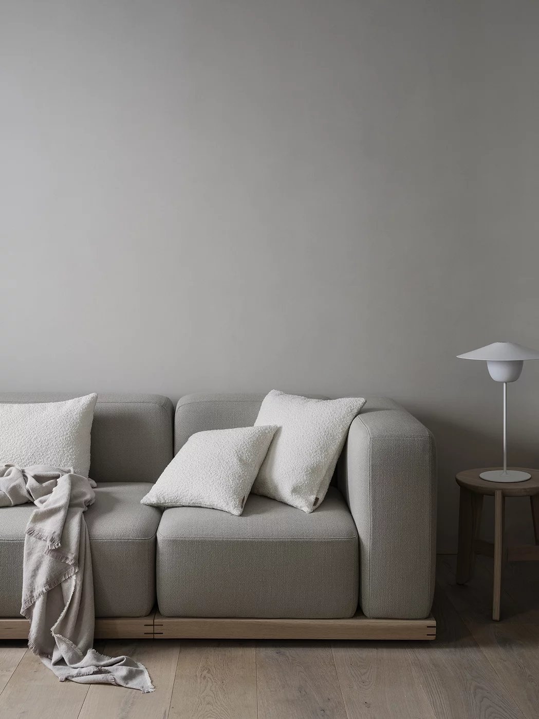 Graues Wohnzimmer mit Sofa, weißen Kissen, Decke und Blomus Eli Hocker als Beistelltisch für eine Lampe.