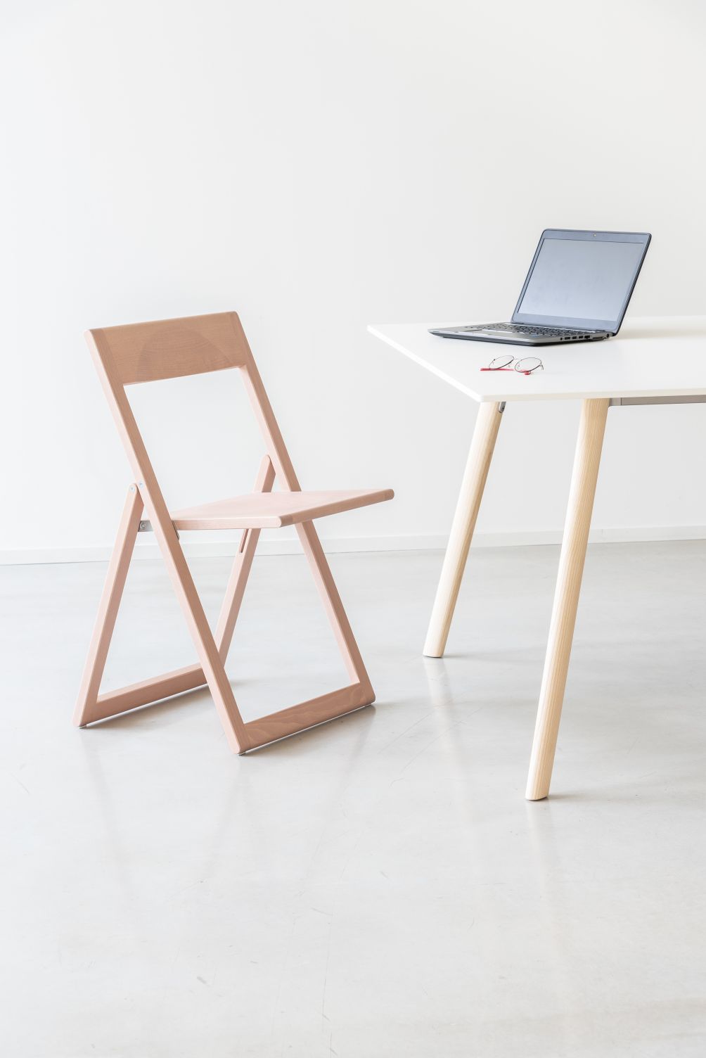 Pilo Tisch Magis mit Laptop und Brille, kombiniert mit einem hellbraunen Holzstuhl, minimalistisches Design.
