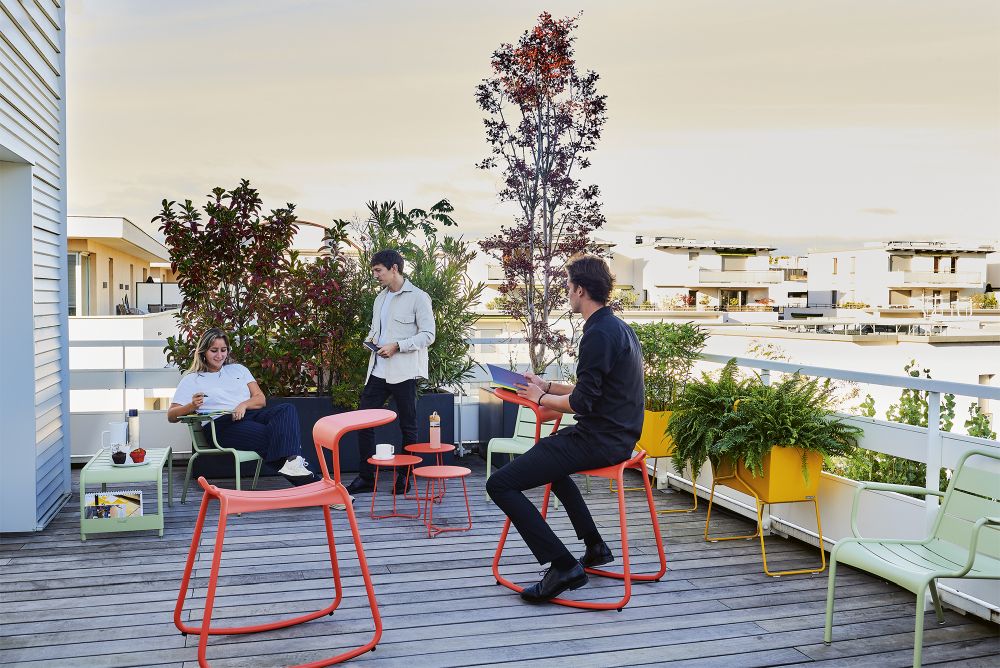 Adadesk Beistelltisch und Fermob Outdoor Möbel auf einer Dachterrasse mit Personen.