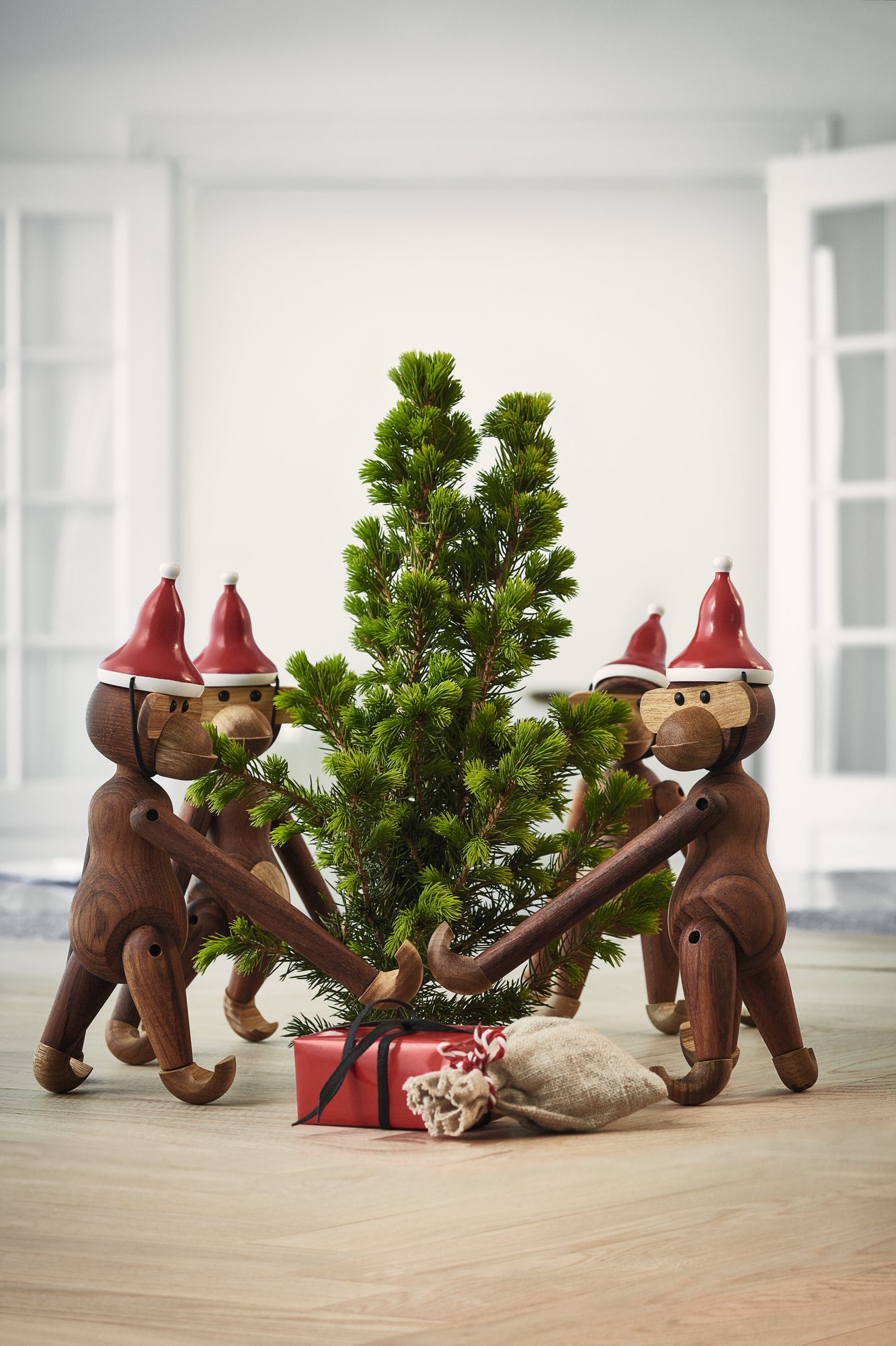 Kay Bojesen Affen mit Weihnachtsmütze um einen kleinen Weihnachtsbaum, Geschenke liegen darunter, festliche Dekoration.