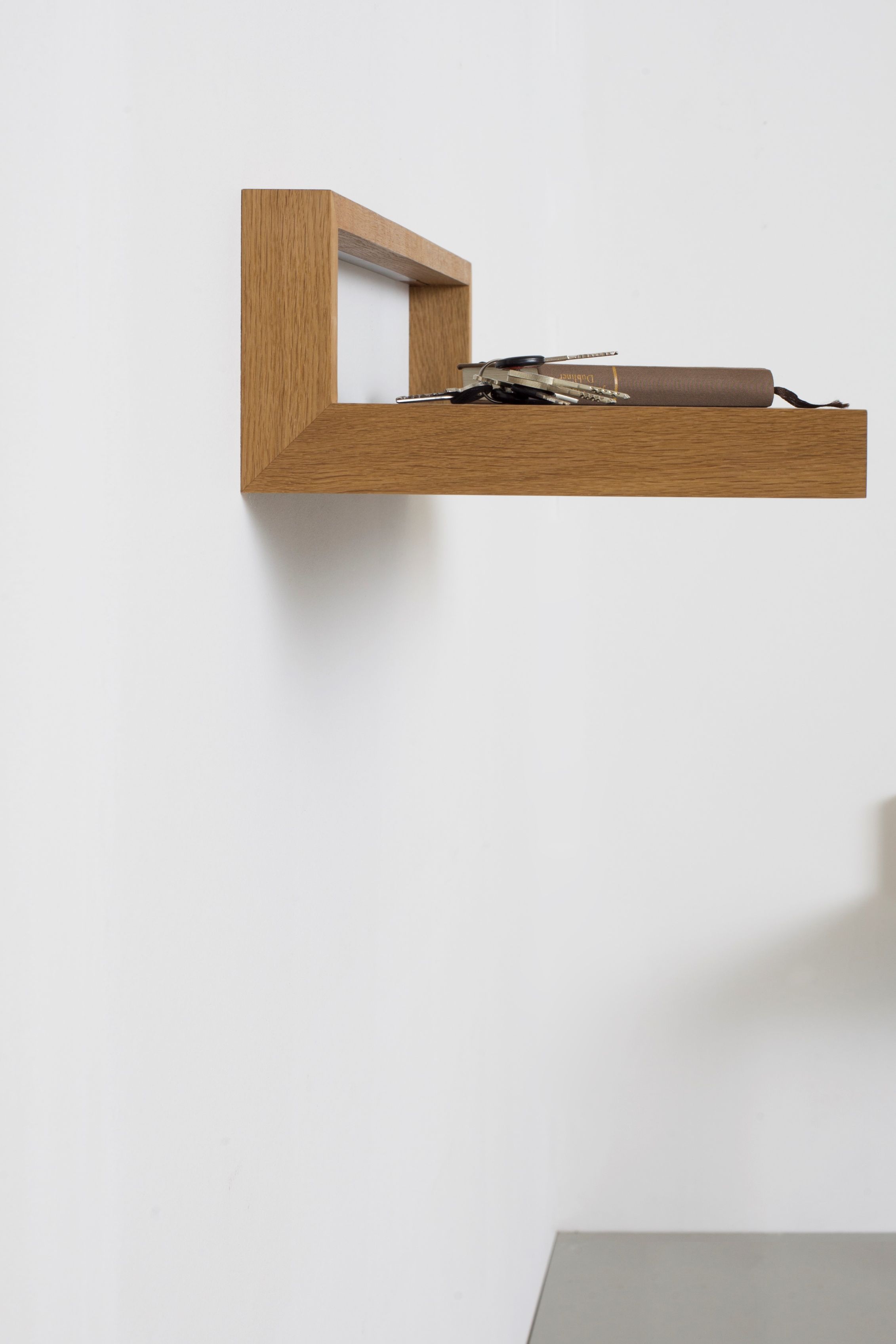 Nahaufnahme des Ablageboards "buck1" mit Schlüssel und Buch an einer weißen Wand.