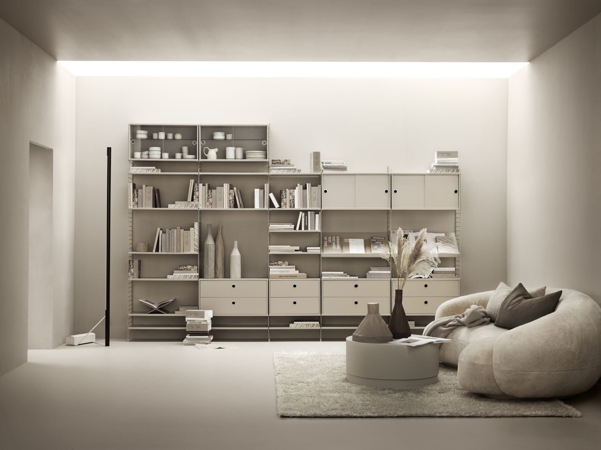 Beiges Wohnzimmer mit modularem Regalsystem, Bücher, Dekoration und gemütlichem Sessel auf einem Teppich.