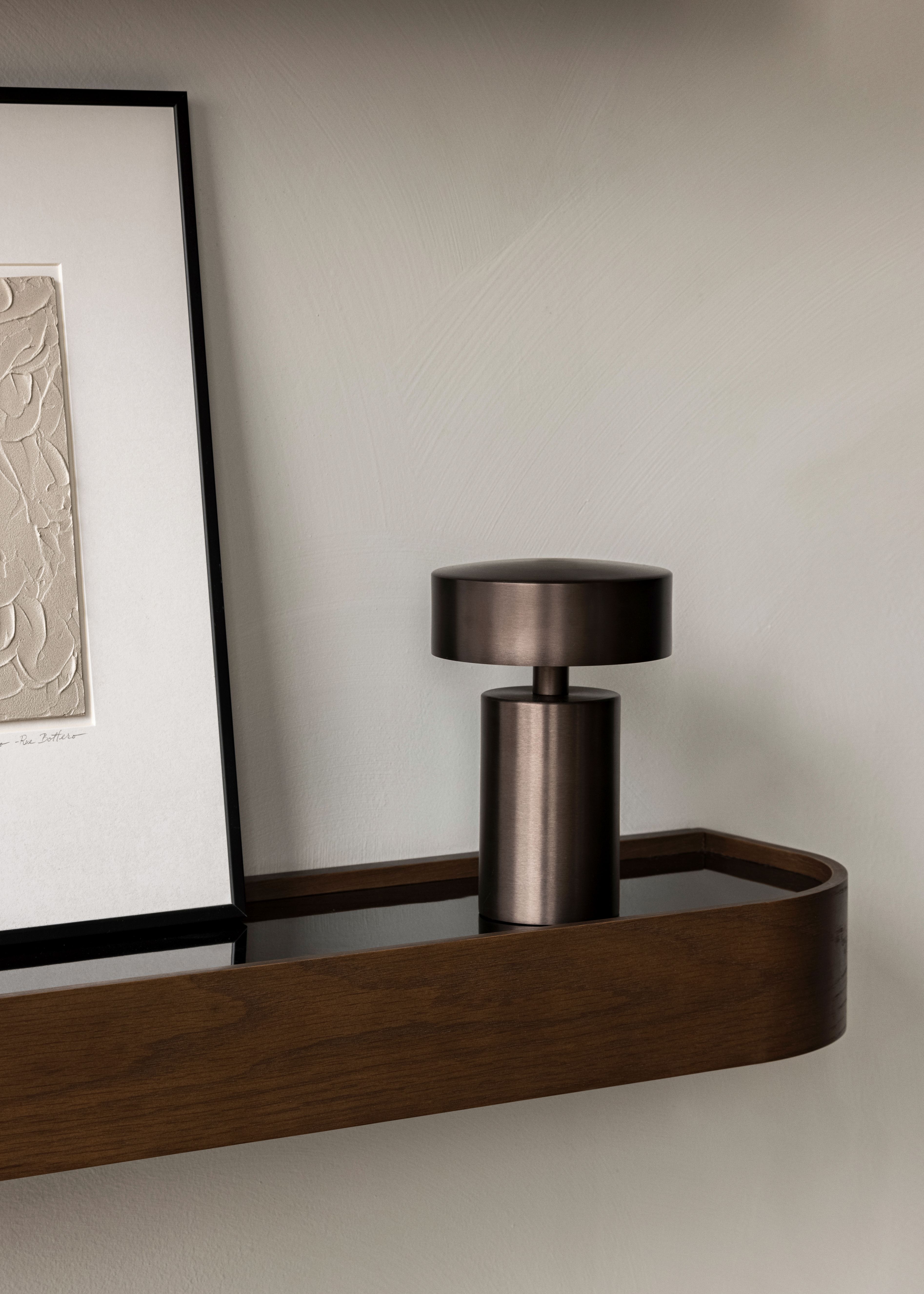 Nahaufnahme der Audo Column Tischleuchte in Bronze auf einem Holzregal. Tragbare Lampe.