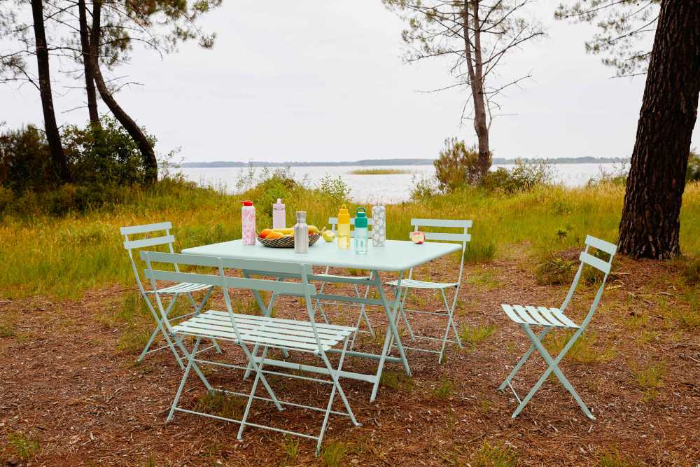 Fermob Bistro Gartenmöbel-Set in Hellblau: Klapptisch, Stühle und Bank für zwei Personen im Freien.