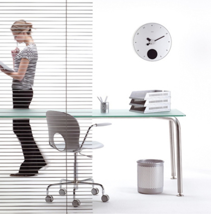 Modernes Büro mit Glas Schreibtisch, Bürostuhl, Papierablage, Pendeluhr und Frau hinter Jalousie.