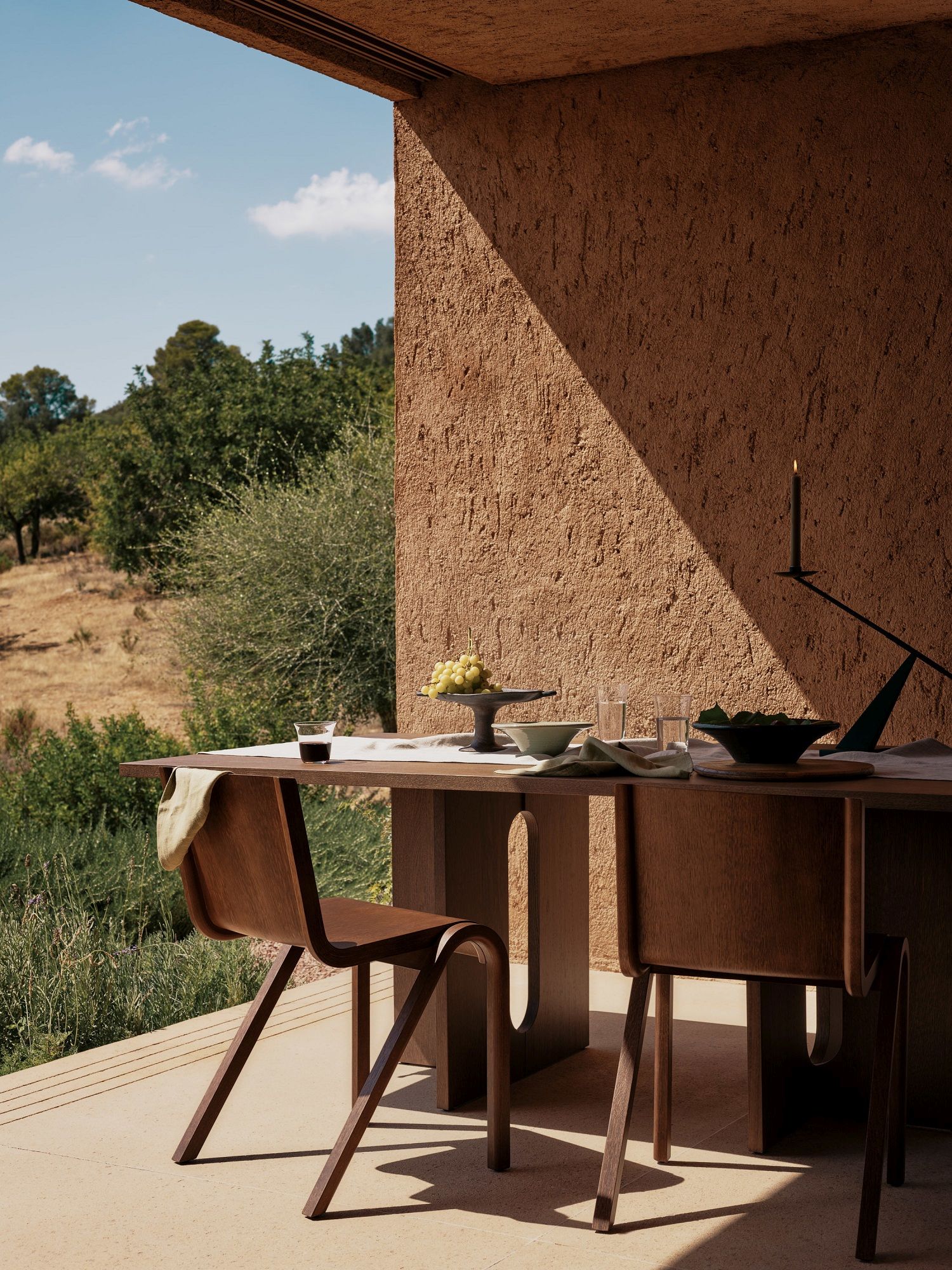 Audo Copenhagen Ready Dining Chair Holzstuhl an Esstisch im Freien mit mediterranem Hintergrund.