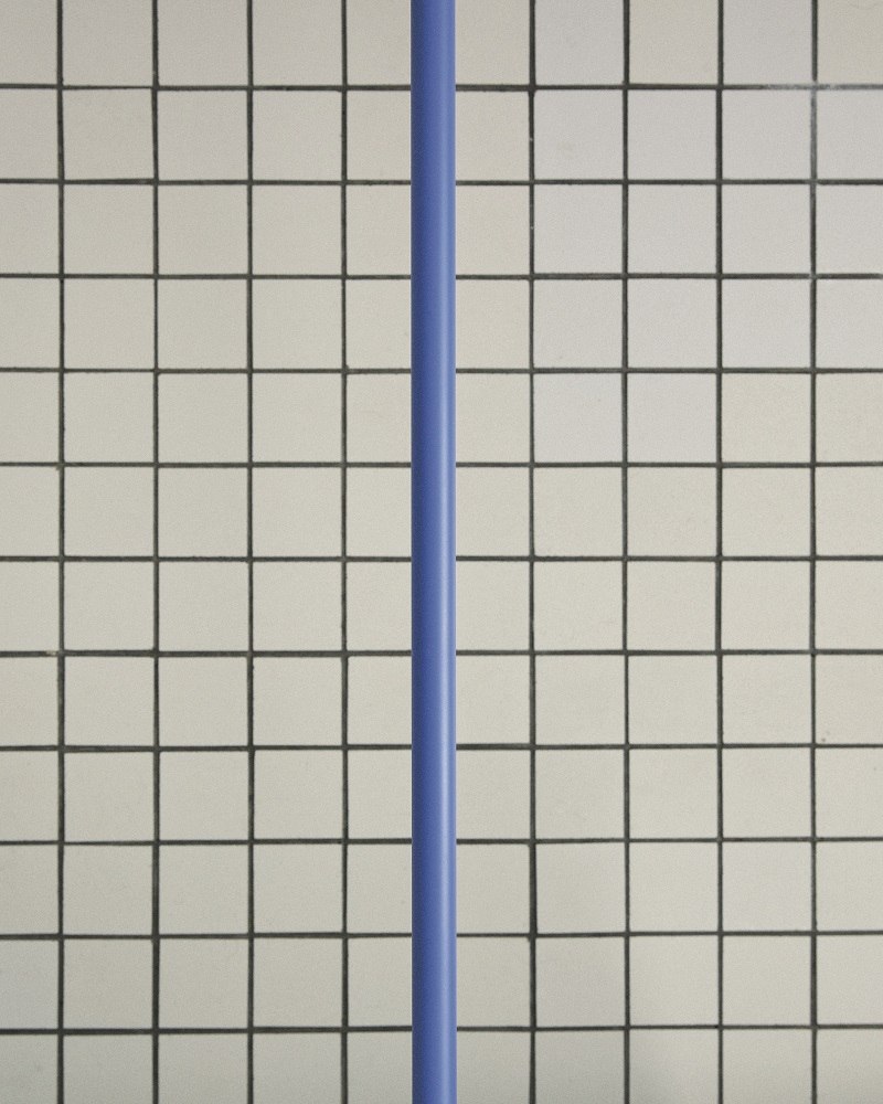 Detailaufnahme der Flos 265 Chromatica Wandleuchte in Blau vor einem quadratischen Fliesenmuster.