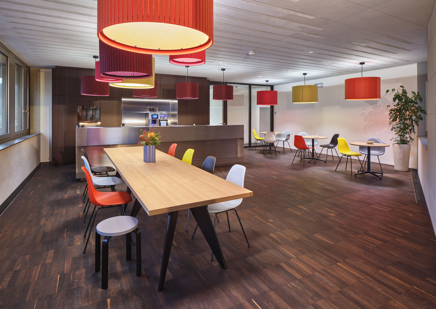 Innenraum mit Holztisch und bunten Eames Plastic Arm Chairs DAX Stühlen von Vitra.