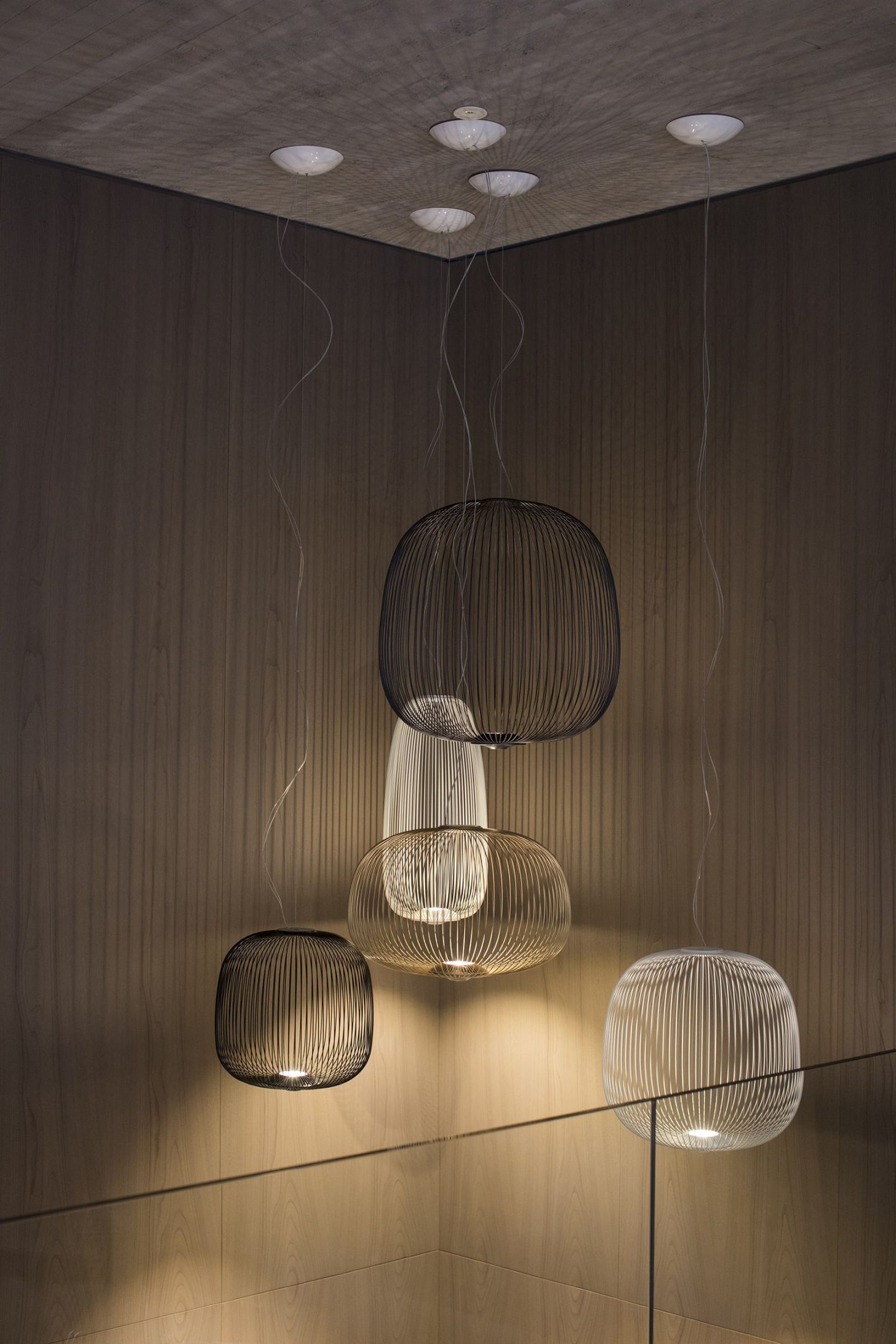 Mehrere Foscarini Spokes Pendelleuchten, darunter eine schwarze, hängen in einem modernen Interieur.