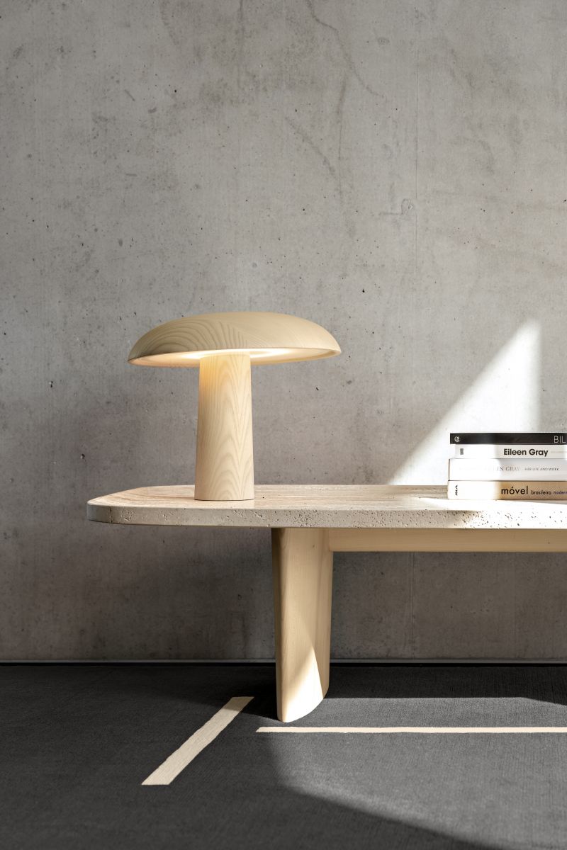 Forma Tischleuchte von ClassiCon aus hellem Holz auf einem Tisch, daneben Bücher.