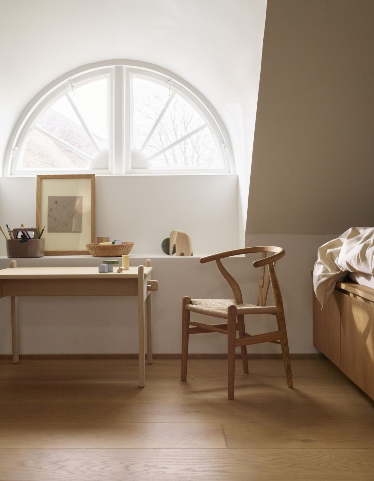 Heller Raum mit Kinderschreibtisch, Spielsachen und einem CH24 Wishbone Stuhl von Carl Hansen & Søn.