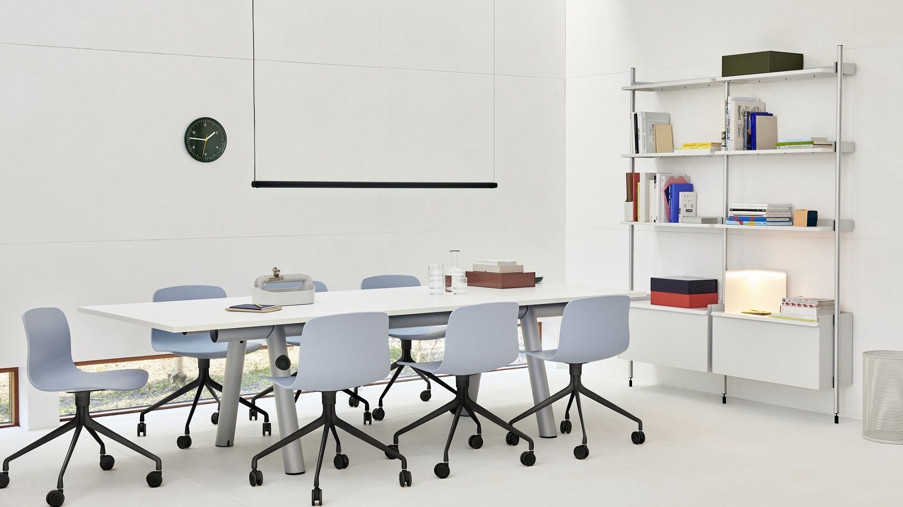 Heller Konferenzraum mit Hay Boa Table Tisch, blauen Stühlen und Regalsystem an der Wand.