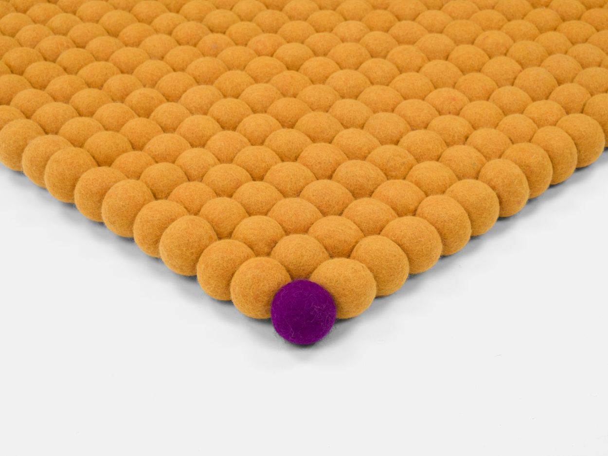 Detailansicht: Ockergelber Filzteppich "Big One" (200x300 cm) aus Filzkugeln, eine violette Kugel.