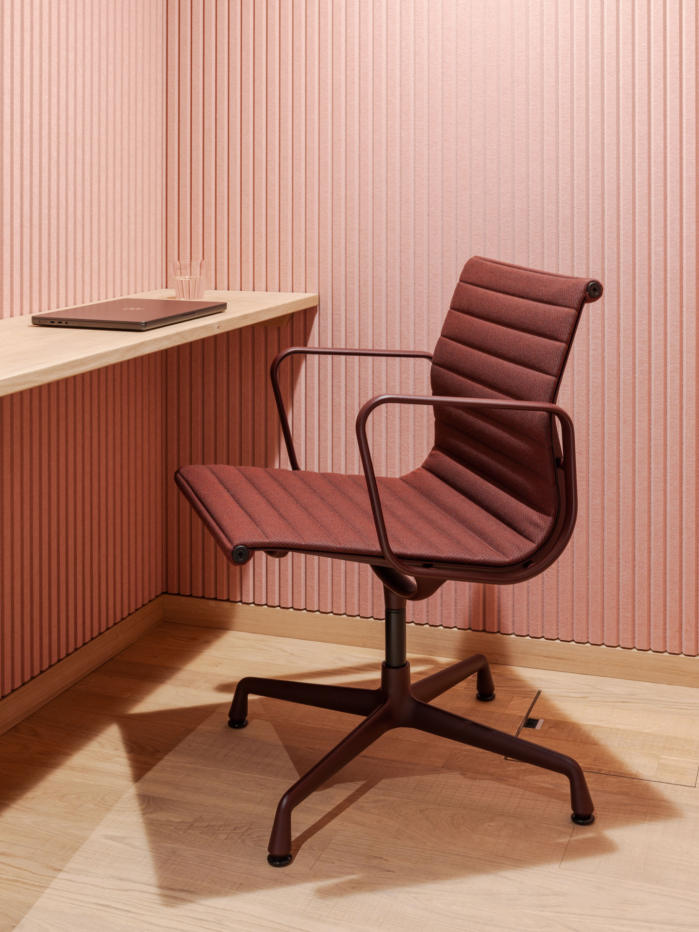 Nahaufnahme eines burgunderroten Vitra EA 108 Aluminium Chair Bürostuhls mit Armlehnen vor rosa Wand.