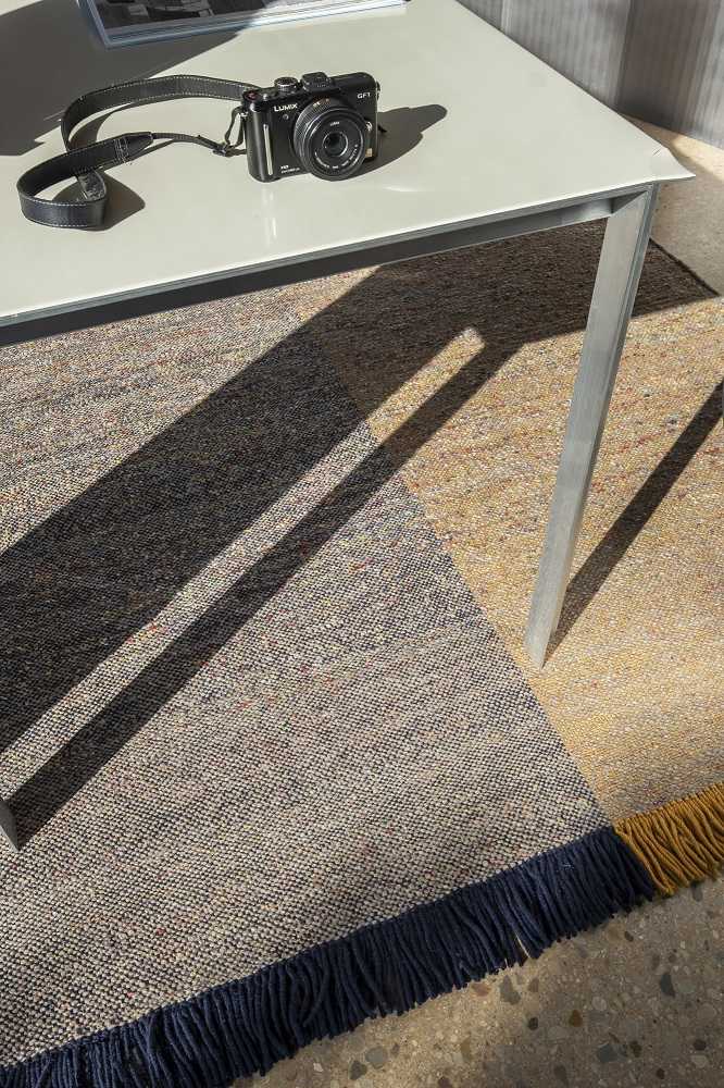 Detailaufnahme des Nanimarquina Re-Rug Teppichs mit blauen Fransen unter einem Tisch, modernes Design.