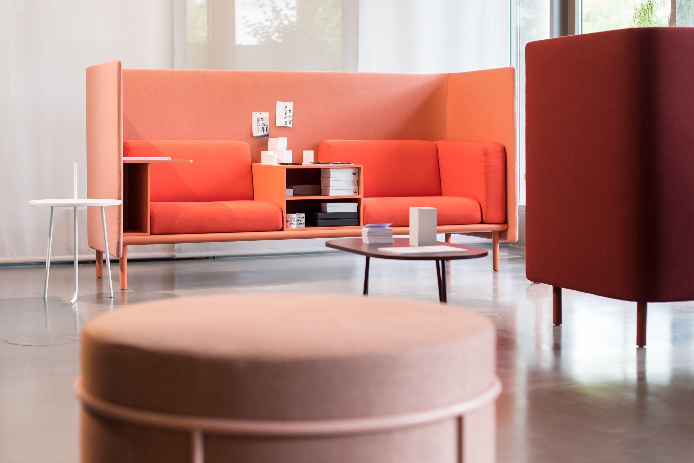Orangefarbenes Cor Floater Sofa mit hohen Seitenwänden, integriertem Regal und kleinem Tisch. Modernes Design für Büro und Wohnraum.