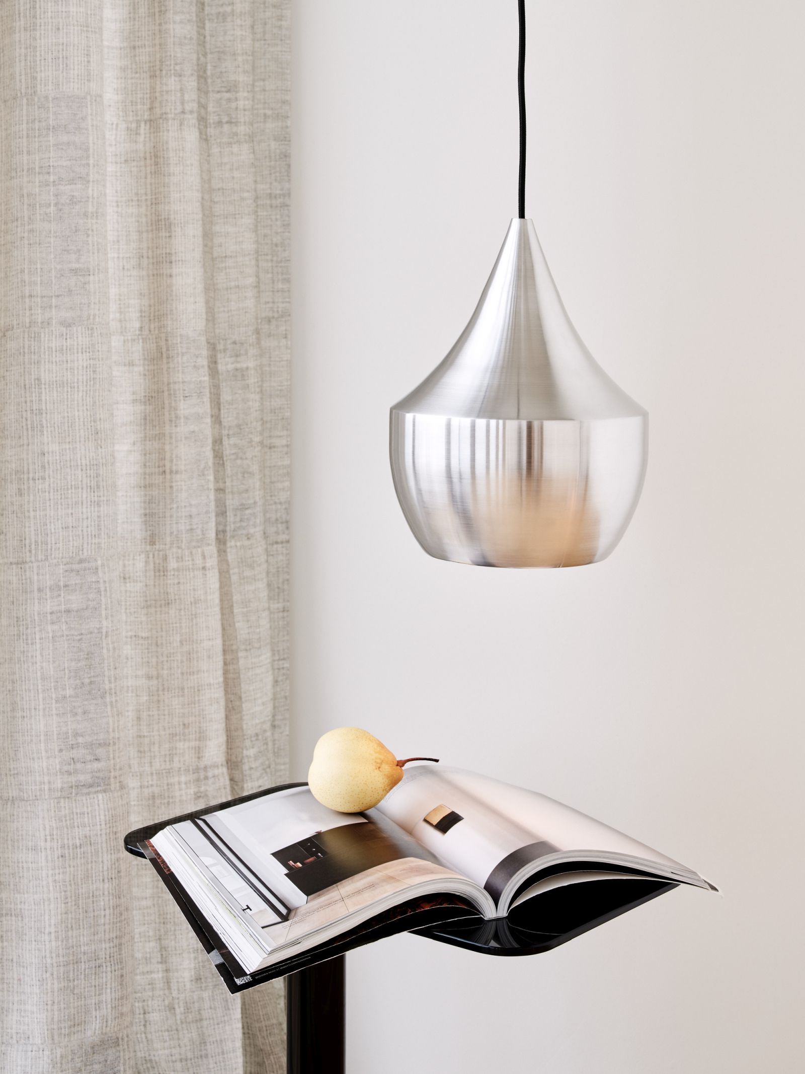 Nahaufnahme der Tom Dixon Fat Pendelleuchte aus gebürstetem Stahl, hängend über einem Magazin mit Birne.