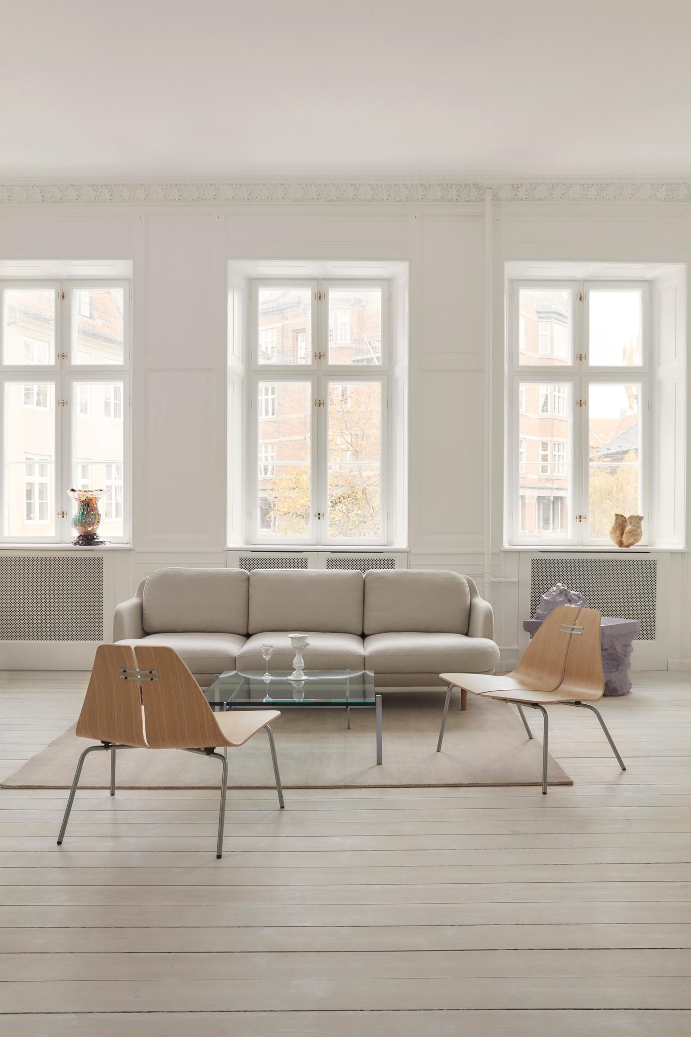 Heller Wohnraum mit PK23 Sessel von Fritz Hansen, Sofa, Glastisch und Teppich auf hellem Holzboden.