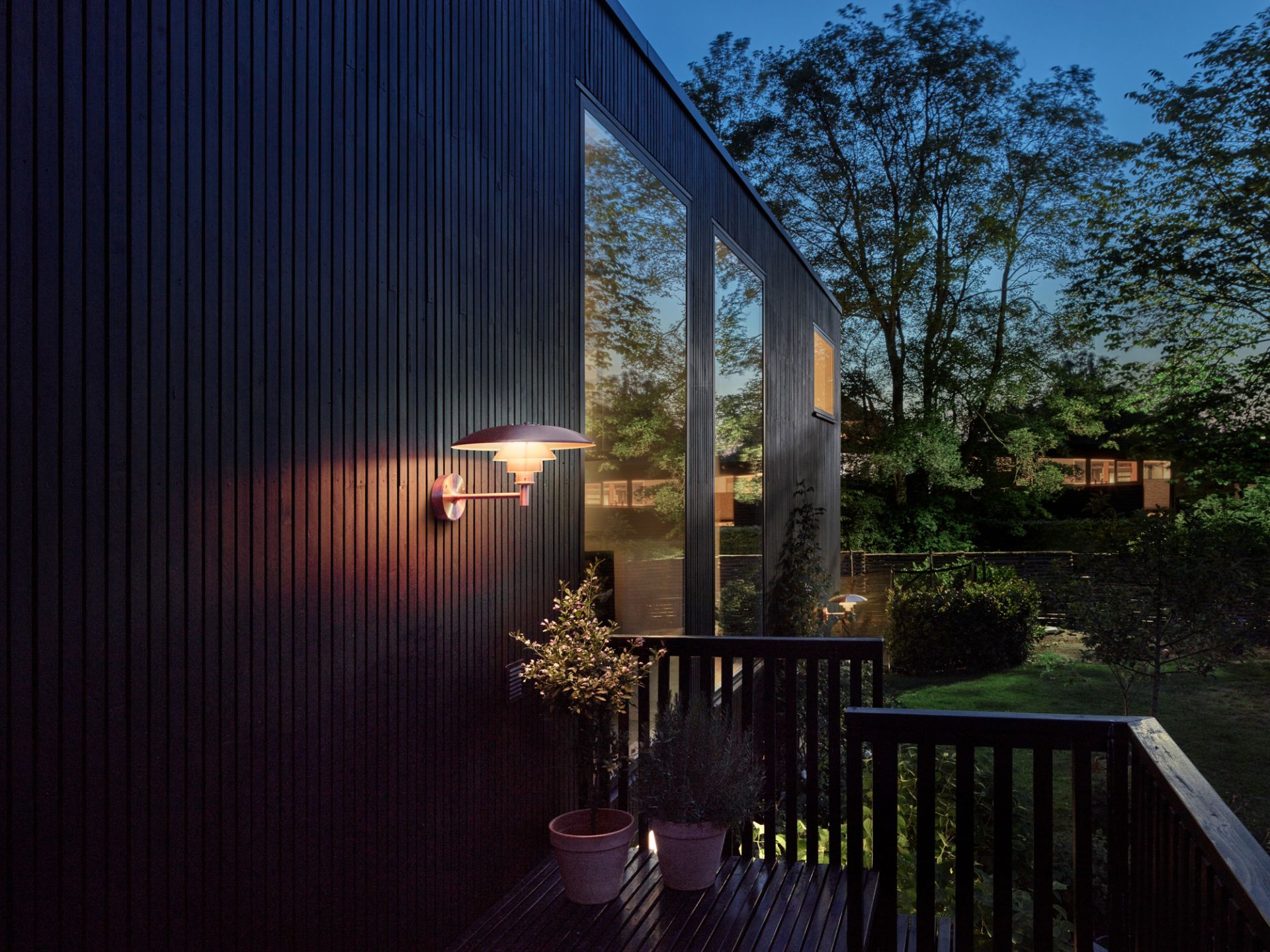 Außenansicht eines Hauses mit einer modernen Wandleuchte, die warmes Licht spendet. Außenbeleuchtung für Haus und Garten.