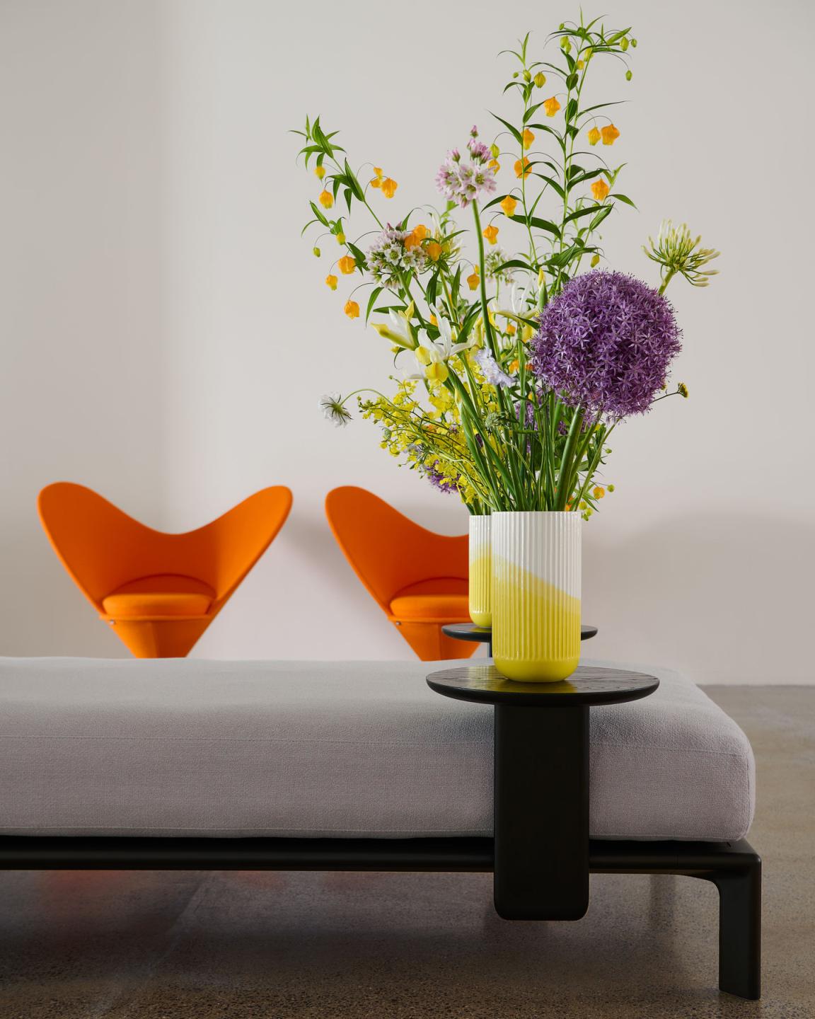 Nahaufnahme des Vitra Anagram Anstecktisches mit Blumen in einer gelb-weißen Vase auf einer grauen Ottomane.
