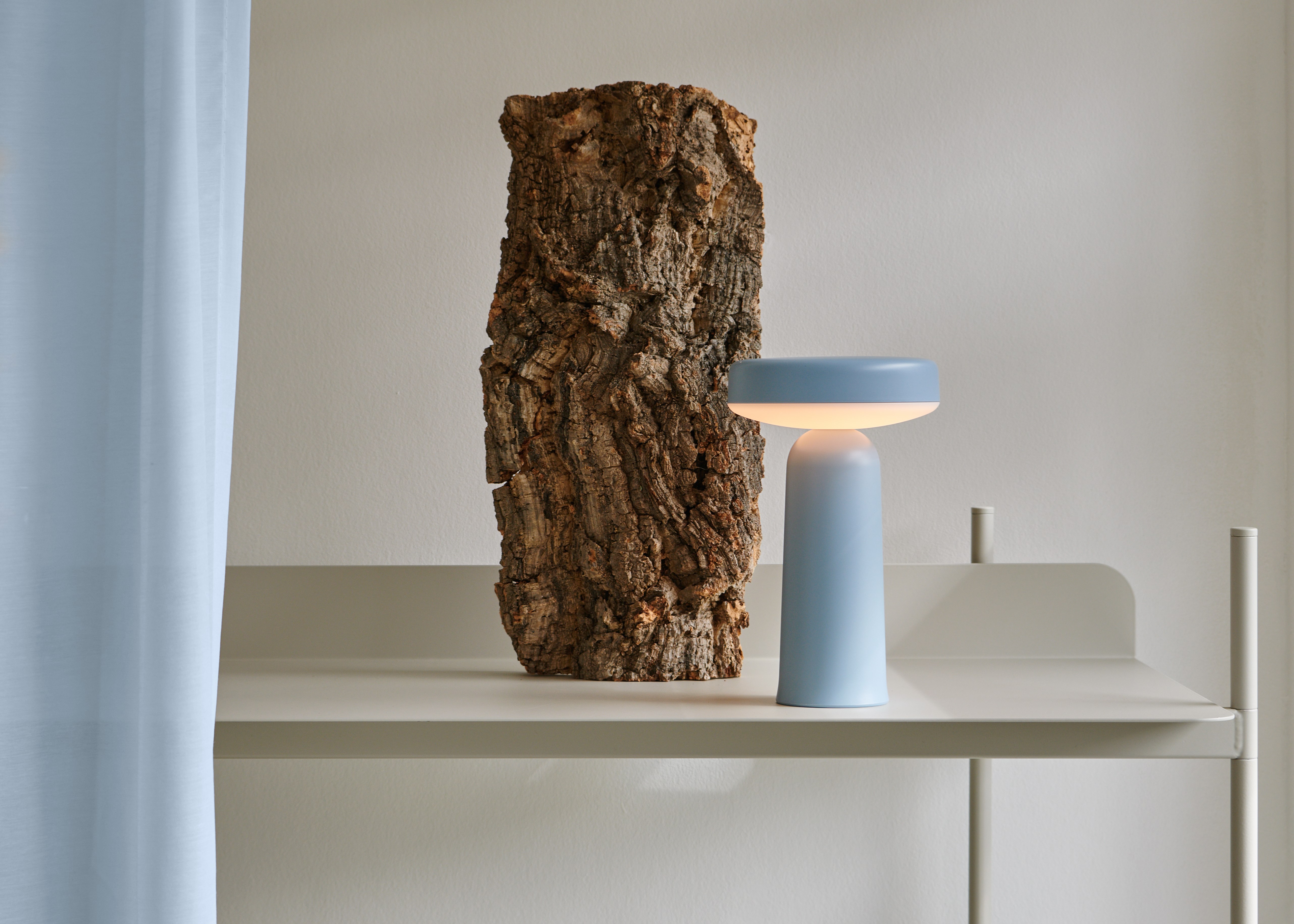 Blaue LED Tischleuchte neben einem Stück Baumrinde auf einem beigen Regal. Moderne Lampe.