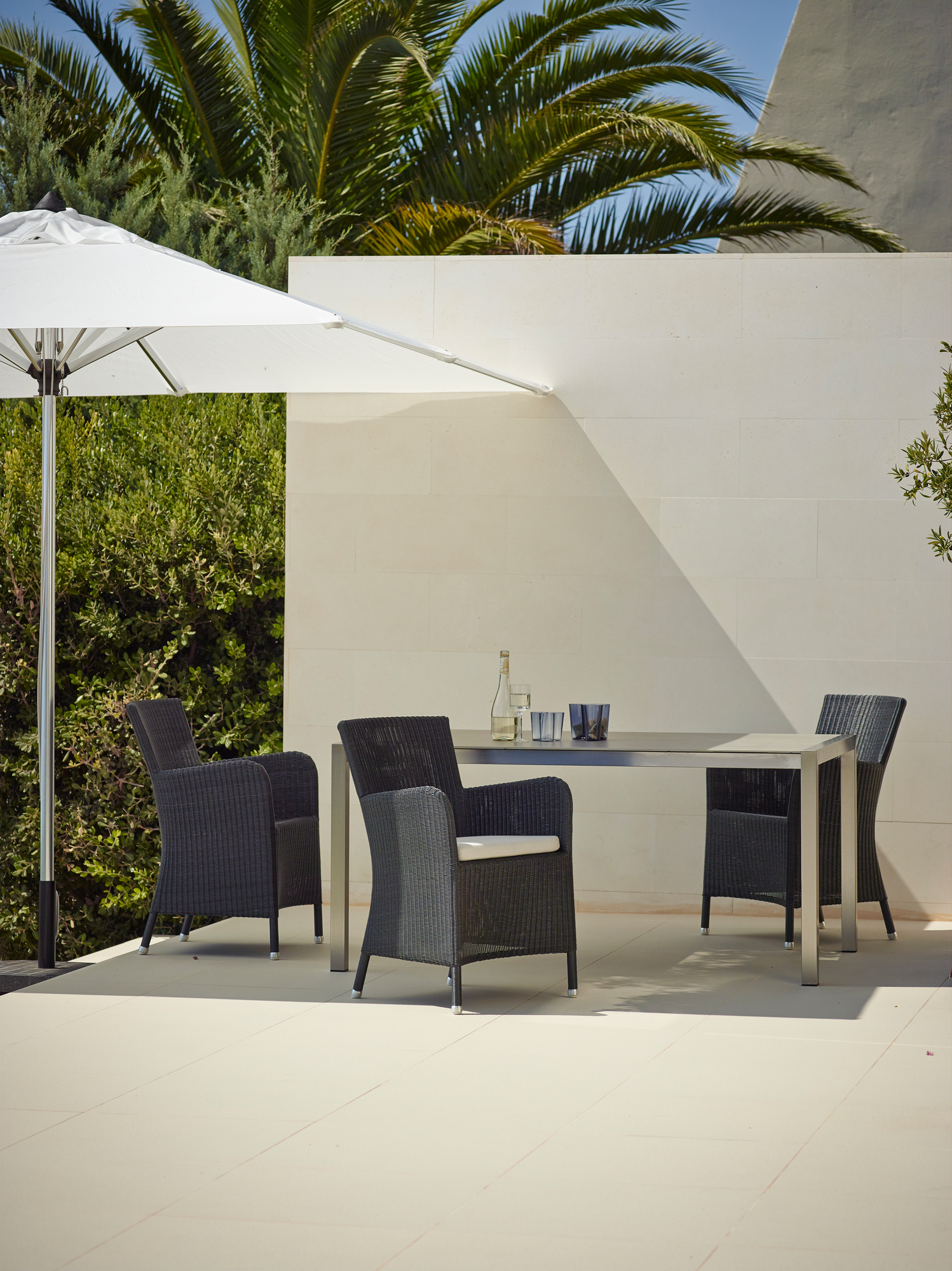 Hampsted Cane-Line Outdoor Sessel aus Rattan mit Tisch und Sonnenschirm auf einer Terrasse.