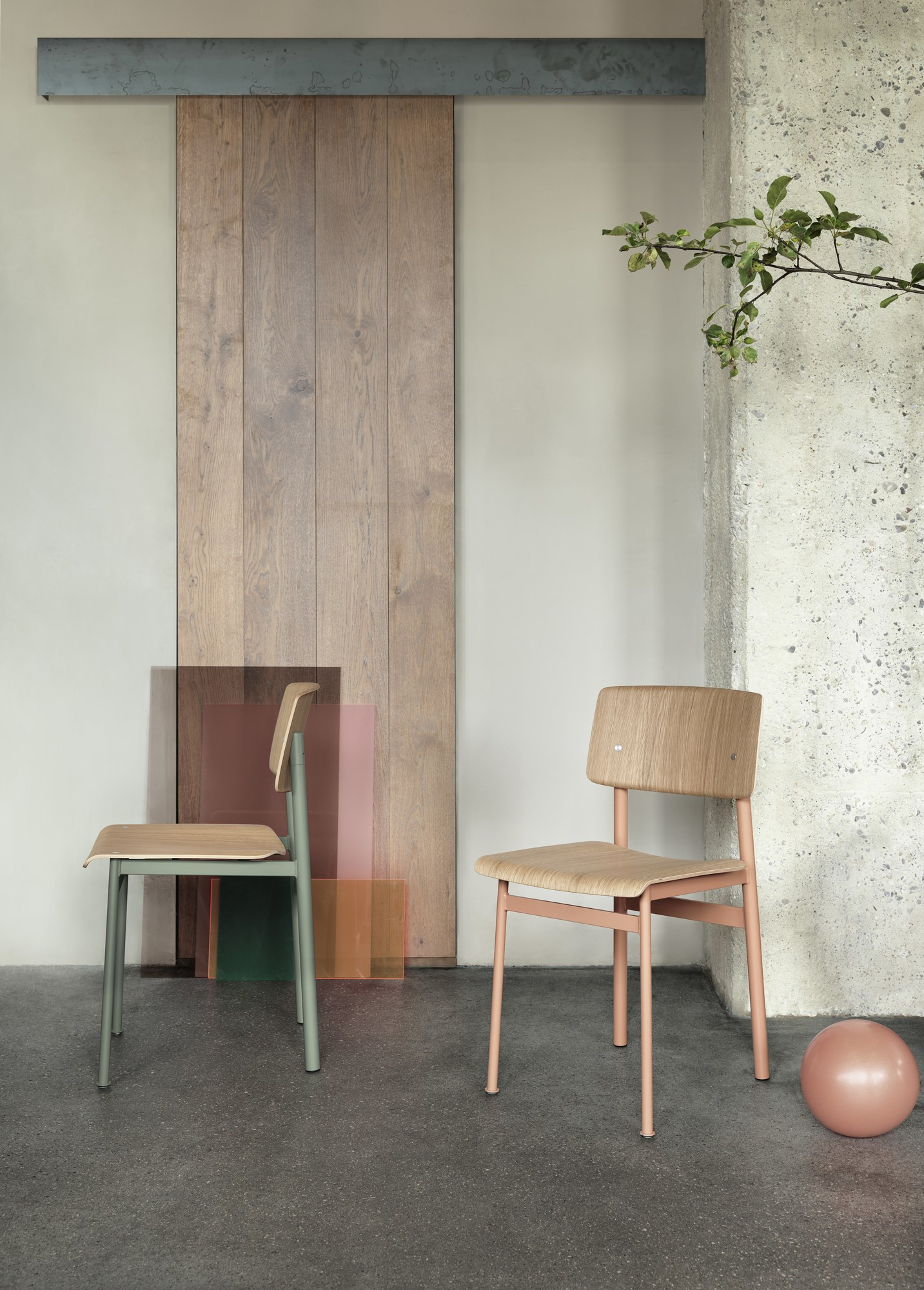Zwei Muuto Loft Chair Stühle in Grün und Rosa vor Holztür und Betonwand.