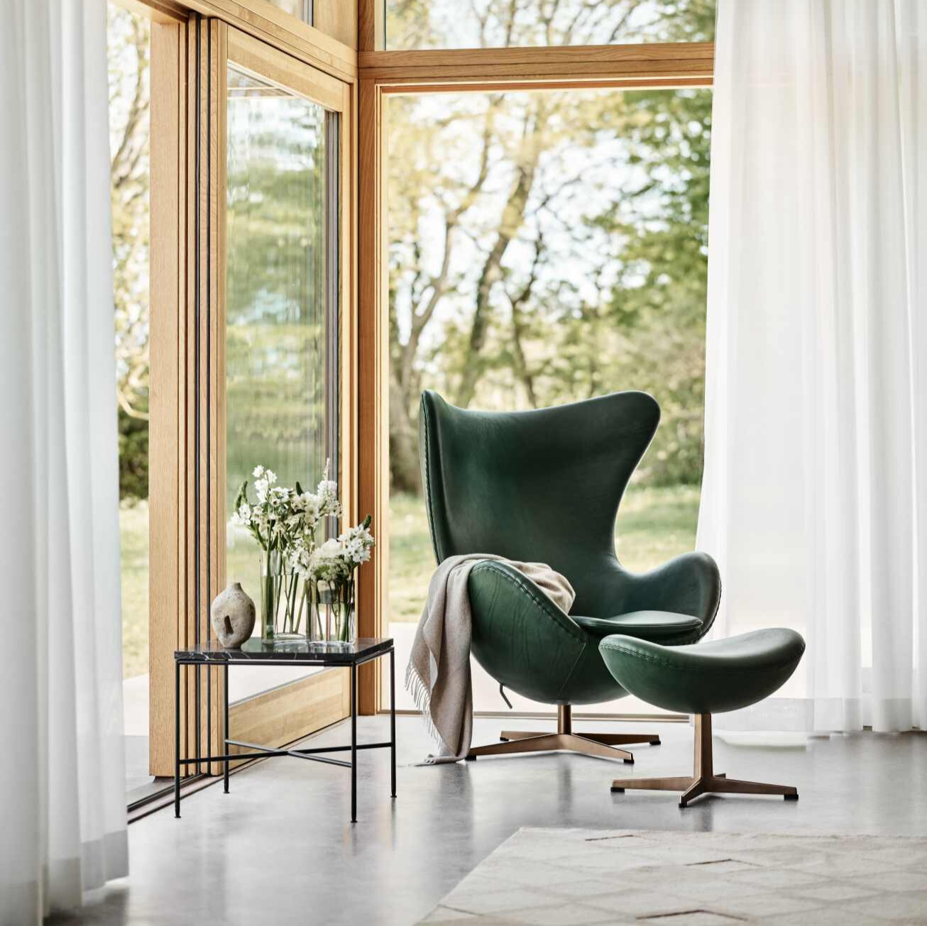Grüner Ledersessel mit Hocker und Beistelltisch in modernem Wohnzimmer mit Fenster und Gartenblick.