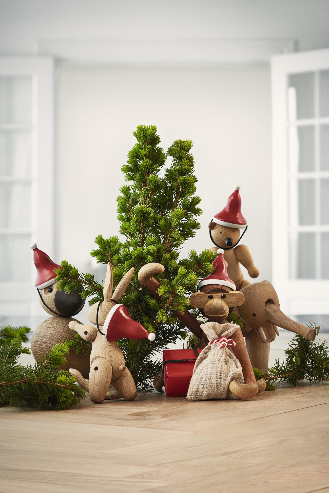 Kay Bojesen Holzfiguren mit Weihnachtsmützen vor einem kleinen Weihnachtsbaum, darunter der kleine Affe mit Weihnachtsmütze.