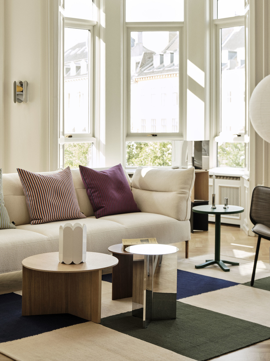 Helles Wohnzimmer mit beigem Sofa, bunten Kissen, Couchtischen und modernem Teppich für stilvolles Wohnen.