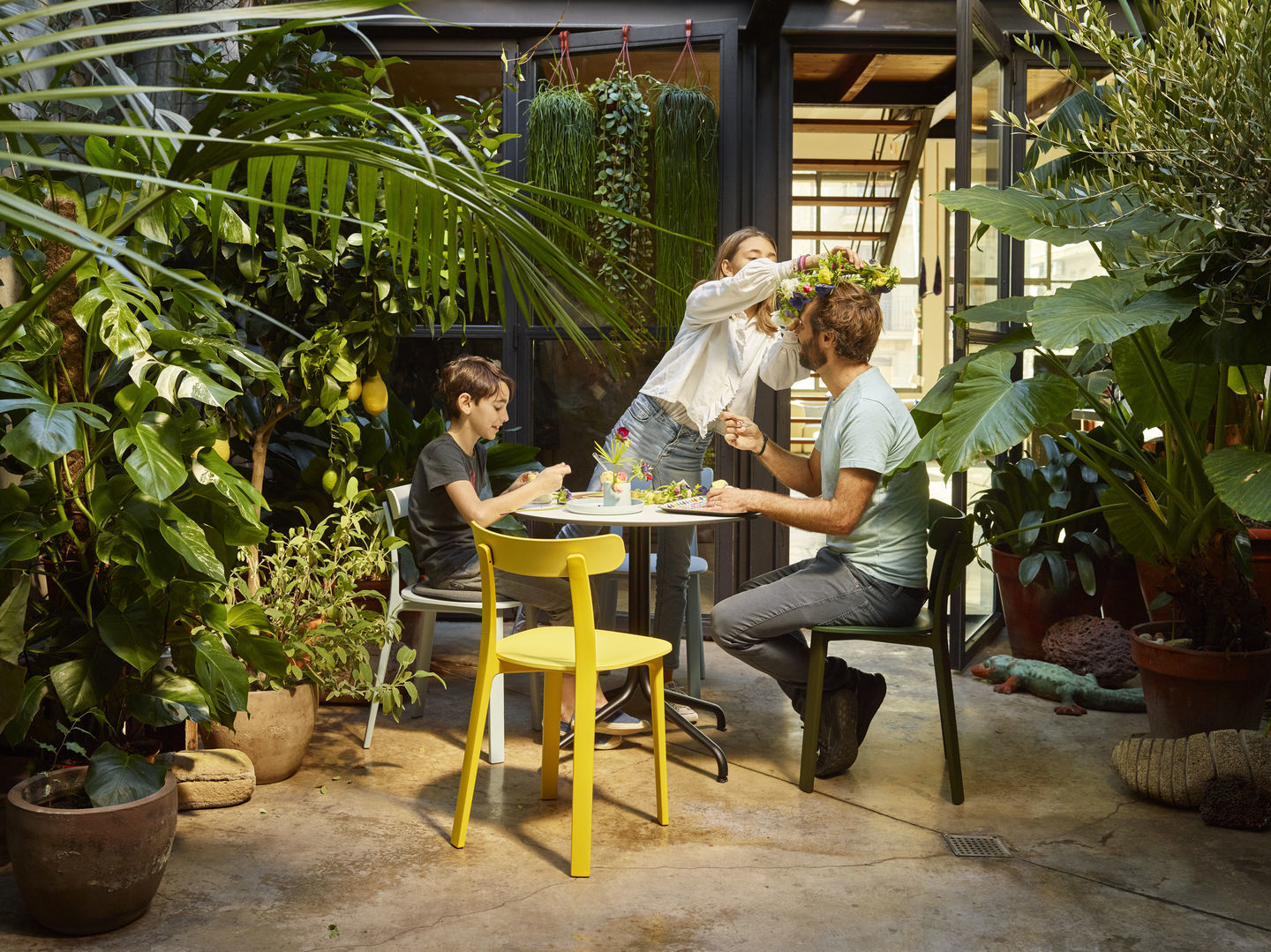 Familie sitzt an Gartentisch auf All Plastic Chairs von Vitra in Gelb und Grün.