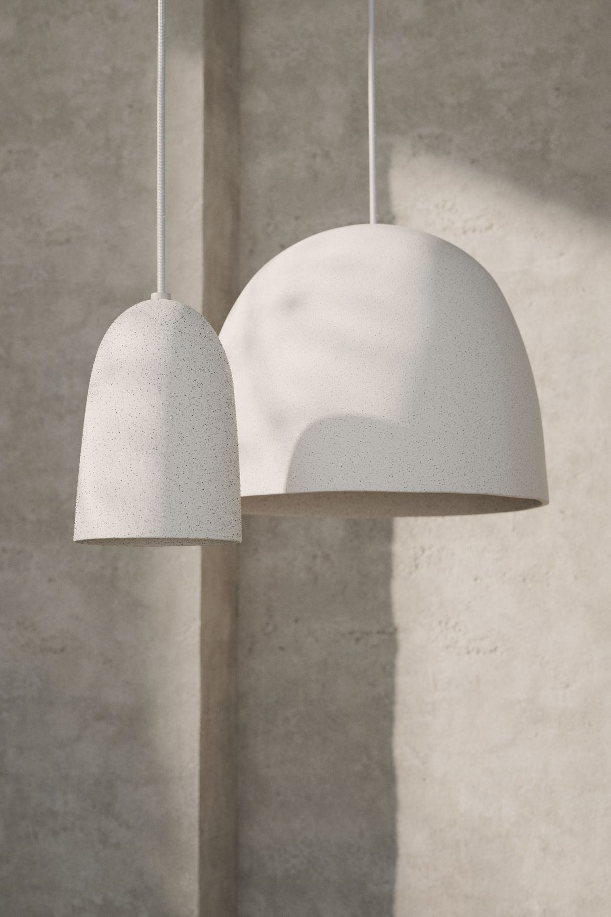 Zwei weiße Speckle Pendelleuchten von Ferm Living in unterschiedlichen Größen hängen vor einer Wand.