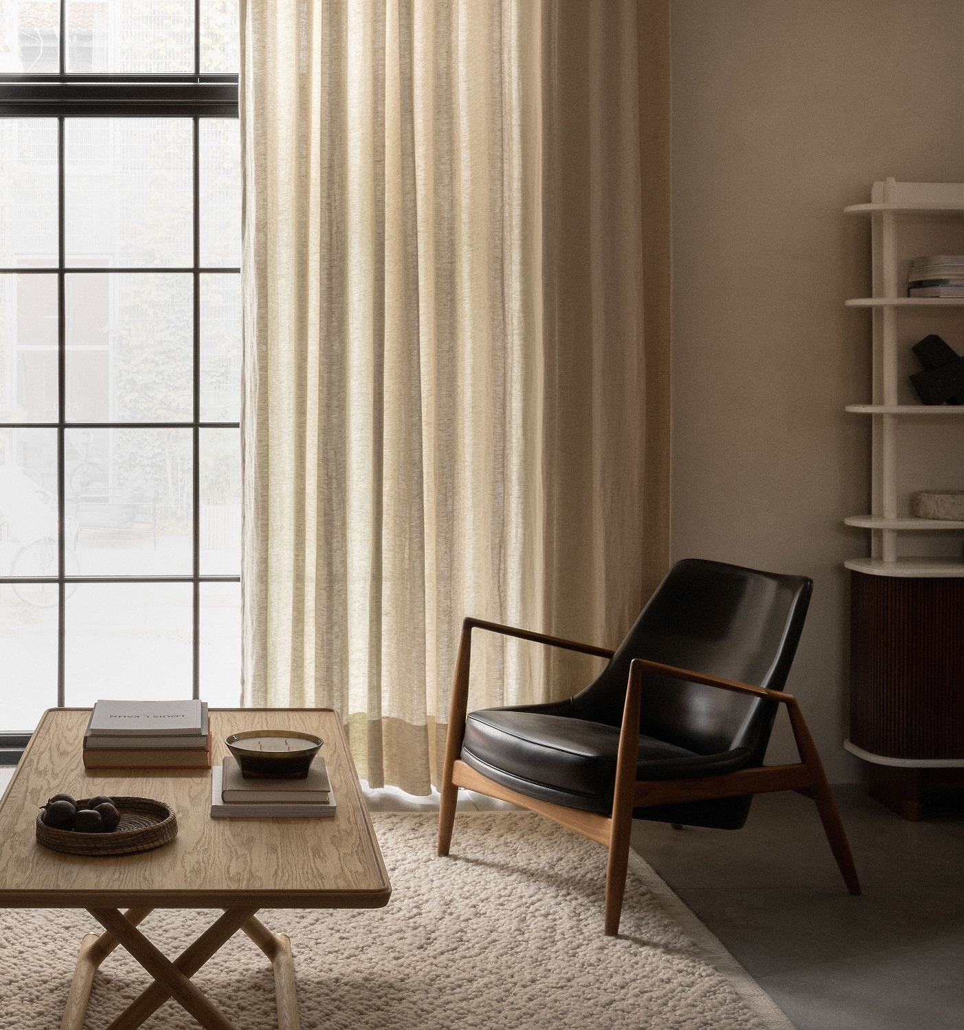 Beiger Audo Copenhagen Gravel Rug Teppich in einem Wohnzimmer mit Sessel und Holztisch.