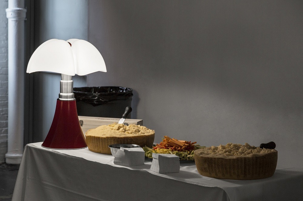 Pipistrello Tischleuchte von Martinelli Luce in Rot auf Tisch mit Käse und Gemüse.