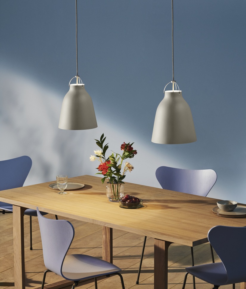 Zwei graue Caravaggio Pendelleuchten von Fritz Hansen über einem Esstisch mit Blumen und Stühlen.
