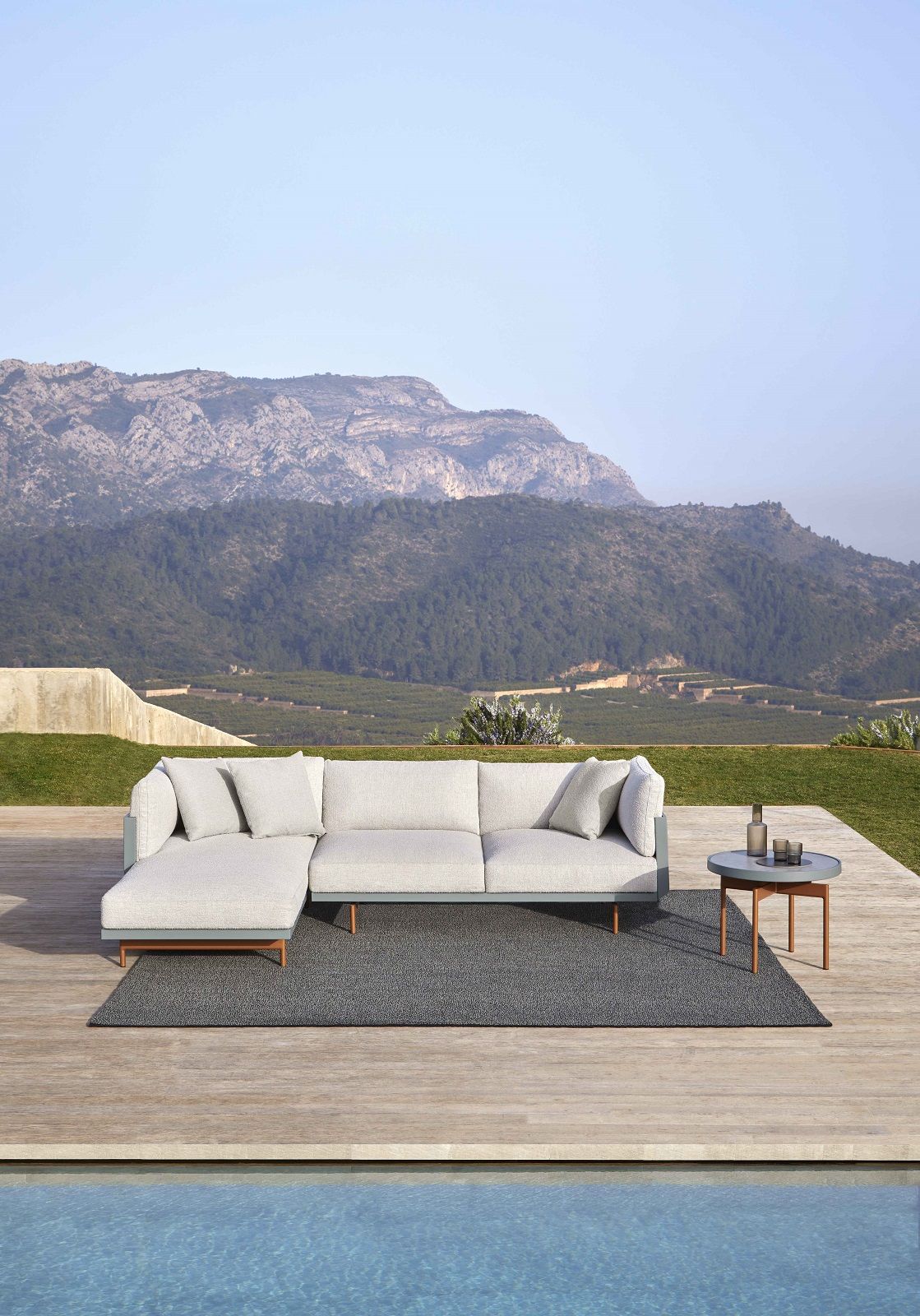 Saline Outdoor Teppich von Gan: Grauer, moderner Outdoor-Teppich unter grauer Lounge-Couch auf Holzterrasse am Pool.